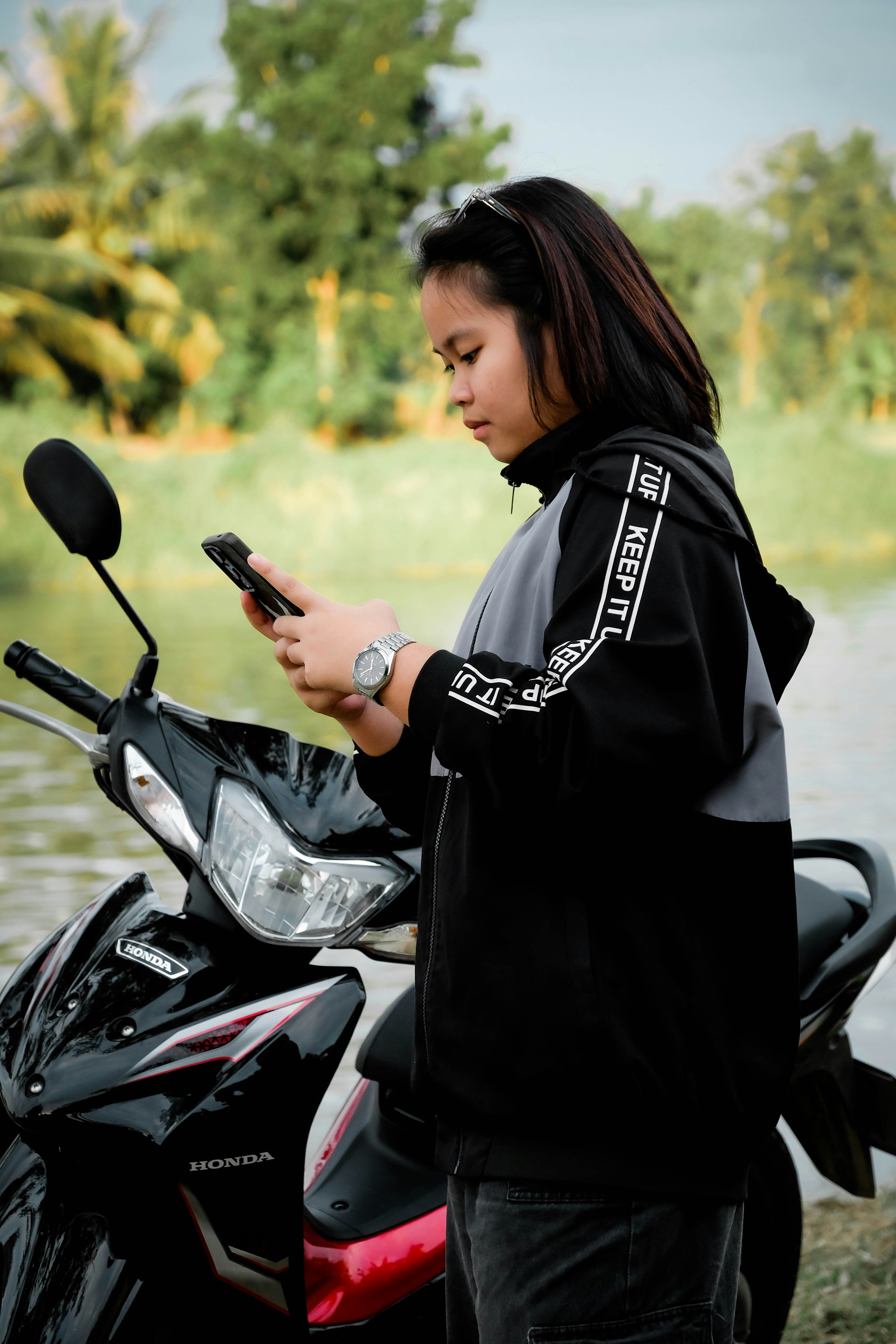 Joven con teléfono junto a una moto cerca del agua