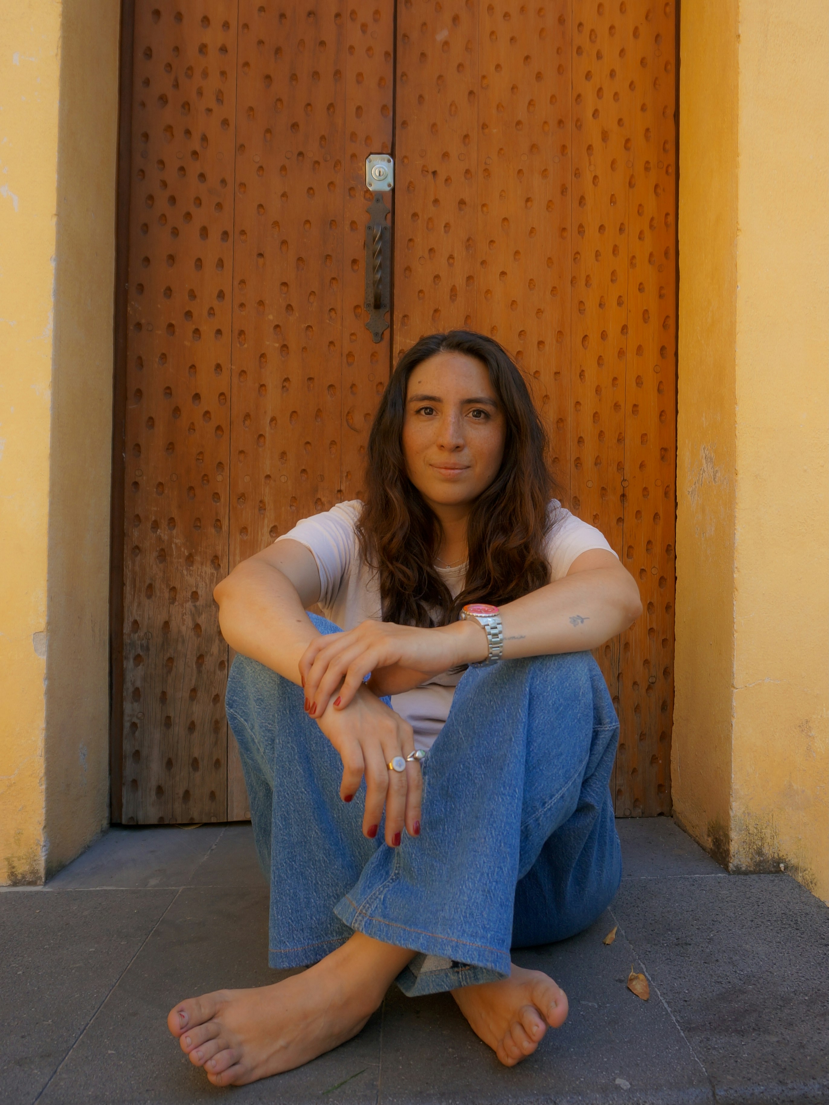 Woman sitting barefoot in front of a wooden door