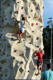 Children climbing a tall artificial rock wall