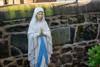 Statue of mary praying against a stone wall.