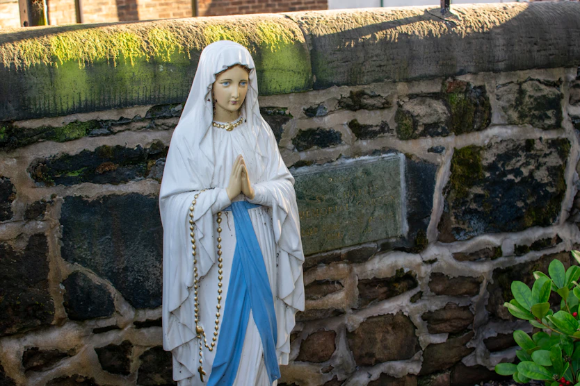 Statue of mary praying against a stone wall.
