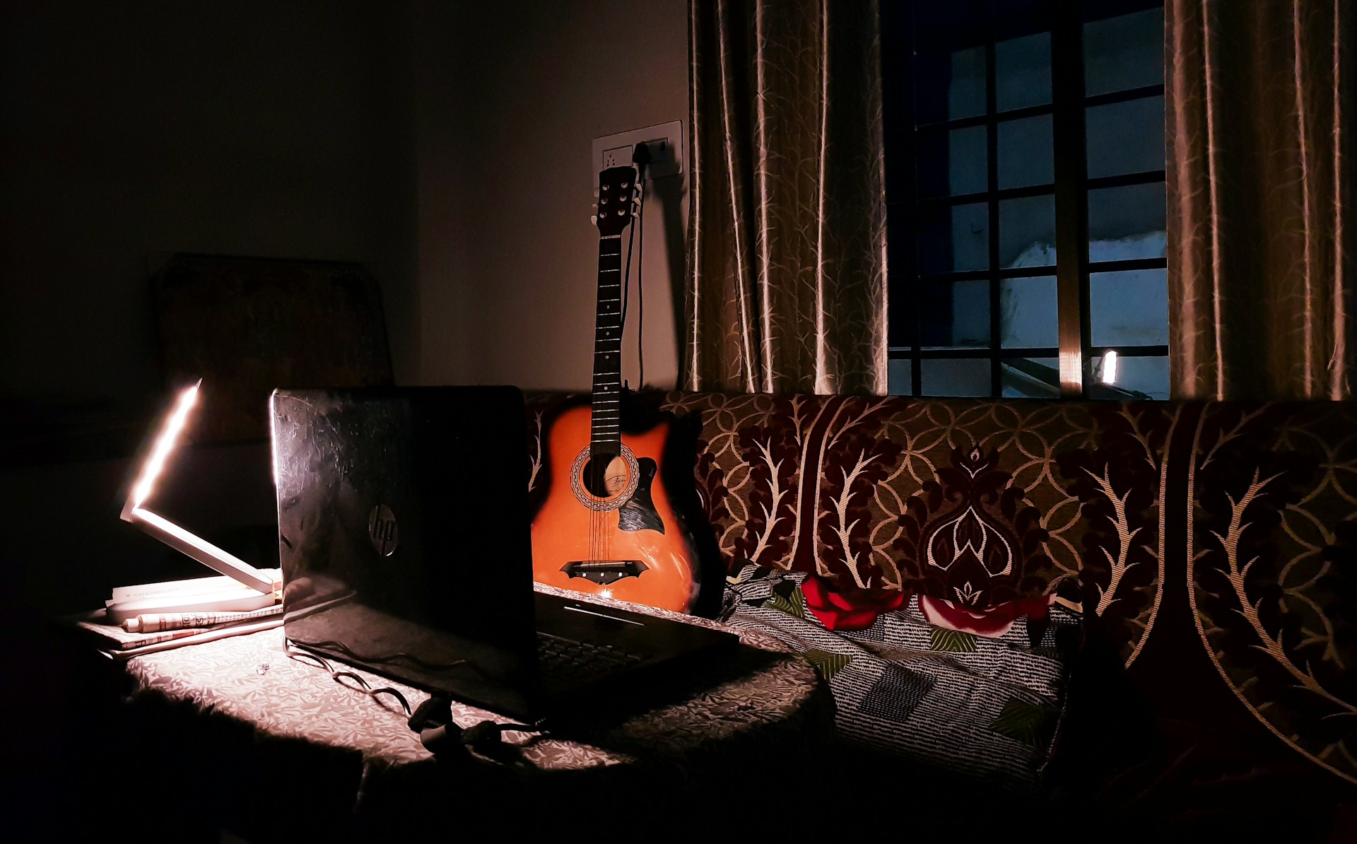 An acoustic guitar rests on a couch near a lamp.