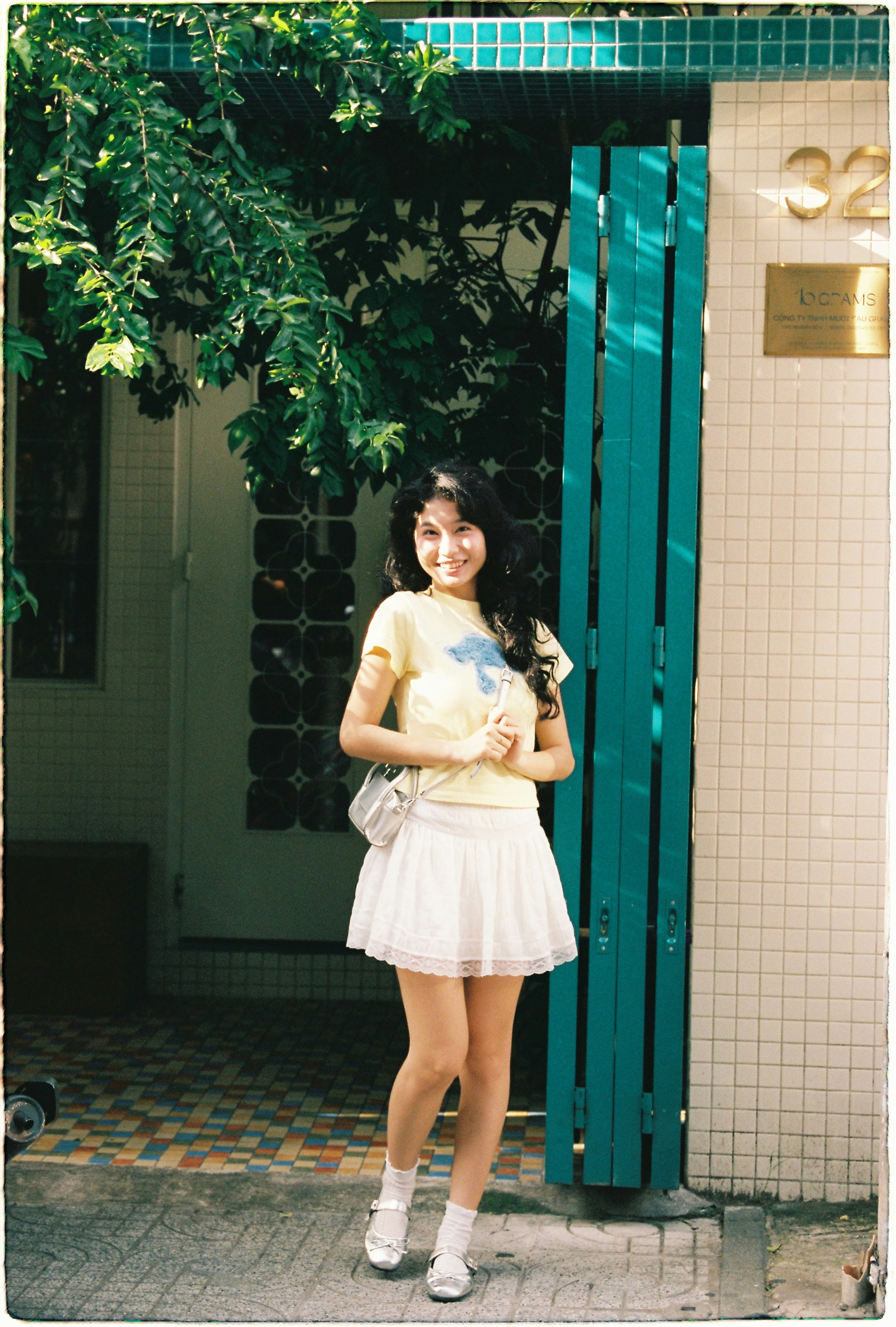 Young woman in yellow shirt and white skirt standing.