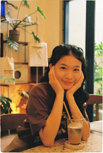 A young woman smiles at a table with a drink.