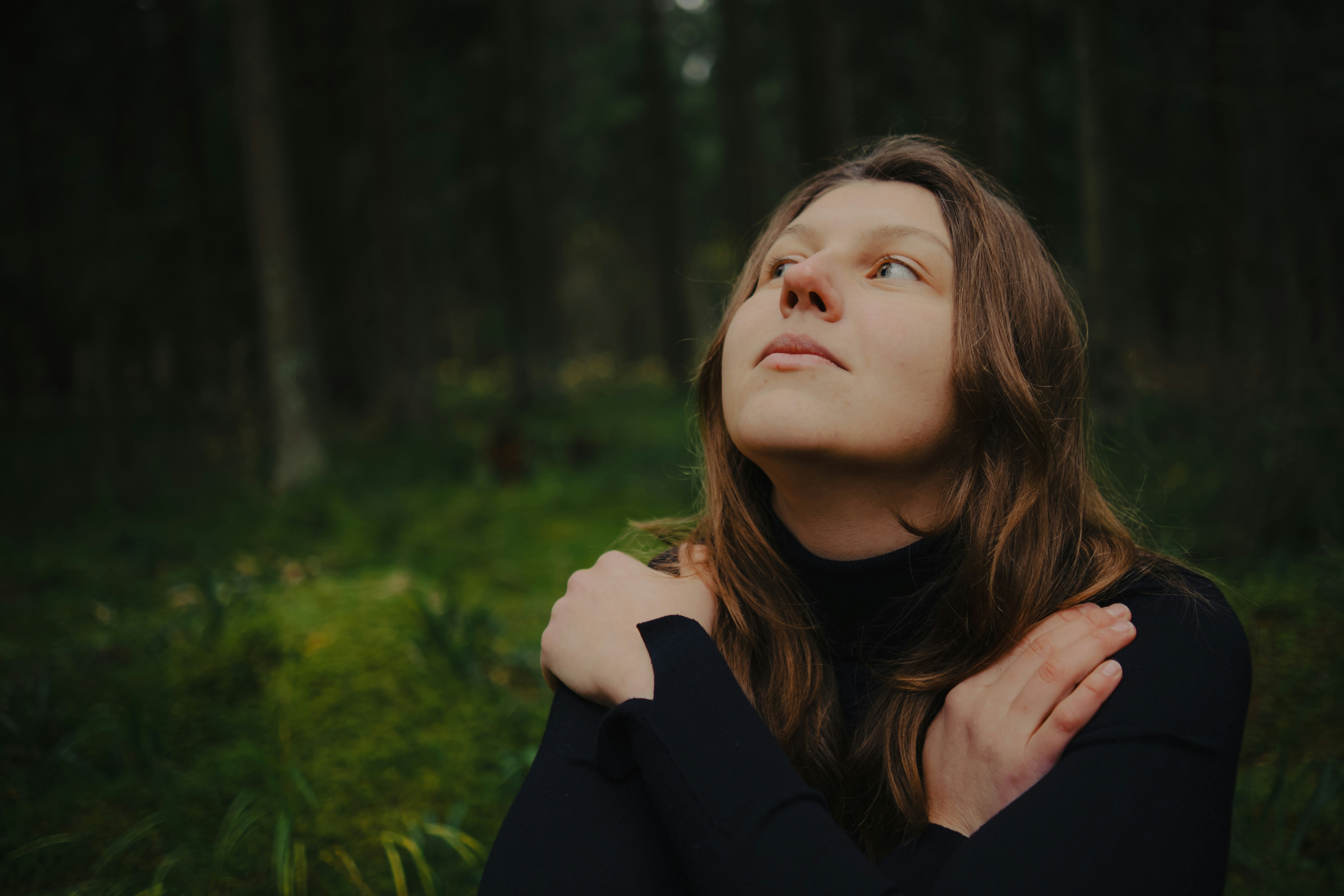 Woman embracing herself in dark forest