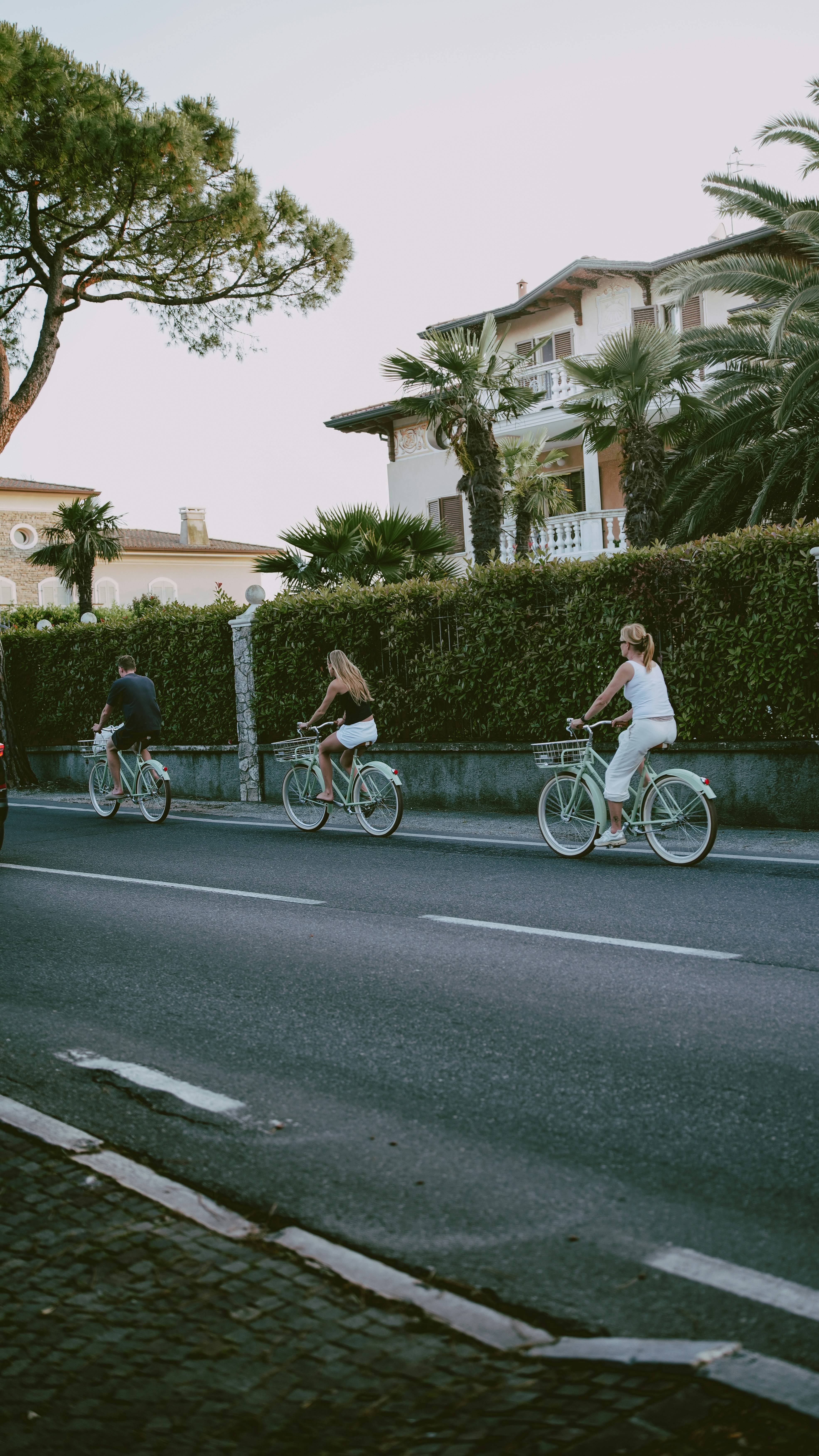 Three people cycling on a road near houses.