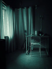 Dimly lit room with desk and chair near window.