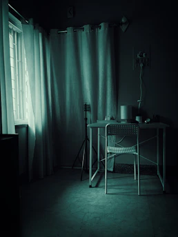 Dimly lit room with desk and chair near window.