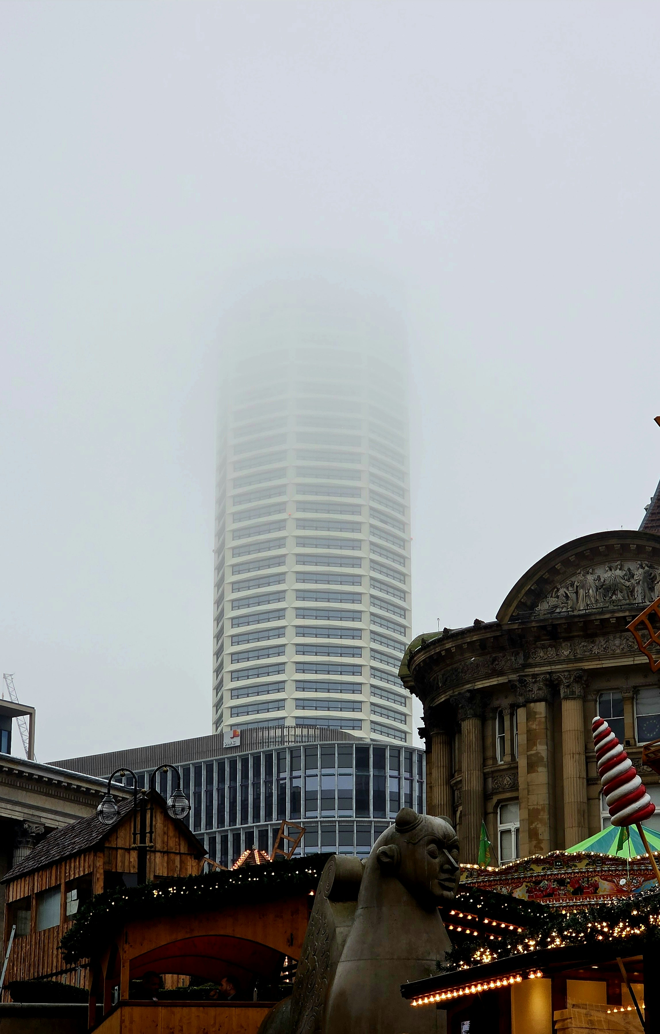 Tall skyscraper partially obscured by fog in city.