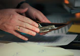 Hands holding cash in a wallet over papers