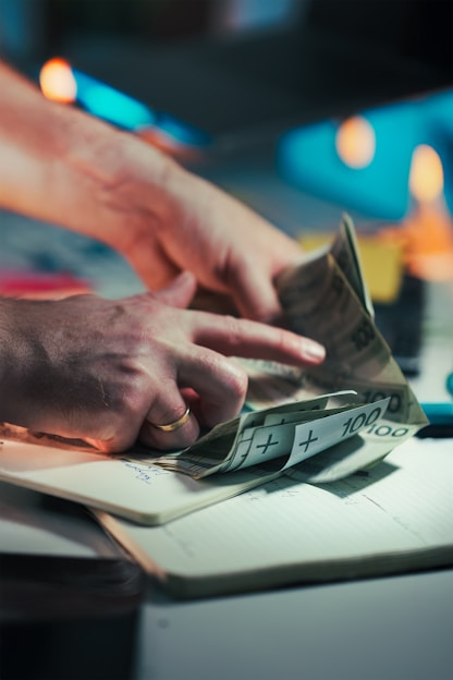 Hands counting polish banknotes on a notebook.