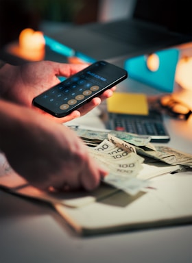 Hands holding money and using calculator on phone.