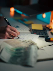 Hand writing in notebook with calculator and cash.
