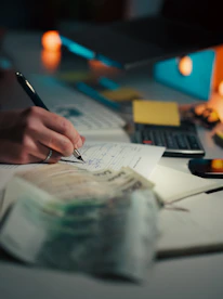 Hand writing in notebook with calculator and cash.
