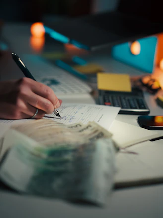 Hand writing in notebook with calculator and cash.
