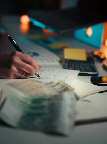Hand writing in notebook with calculator and cash.
