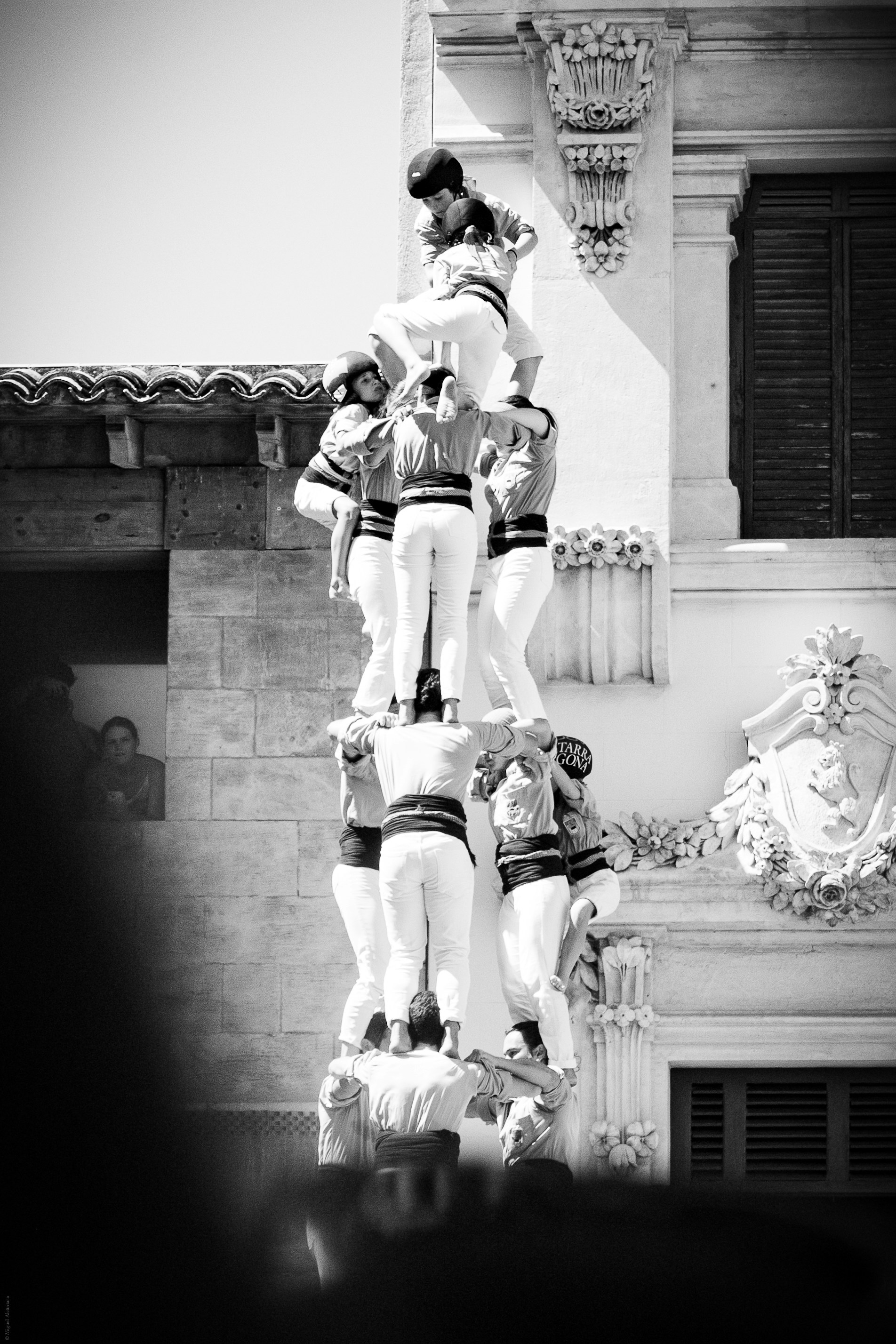People forming a human tower against a building.