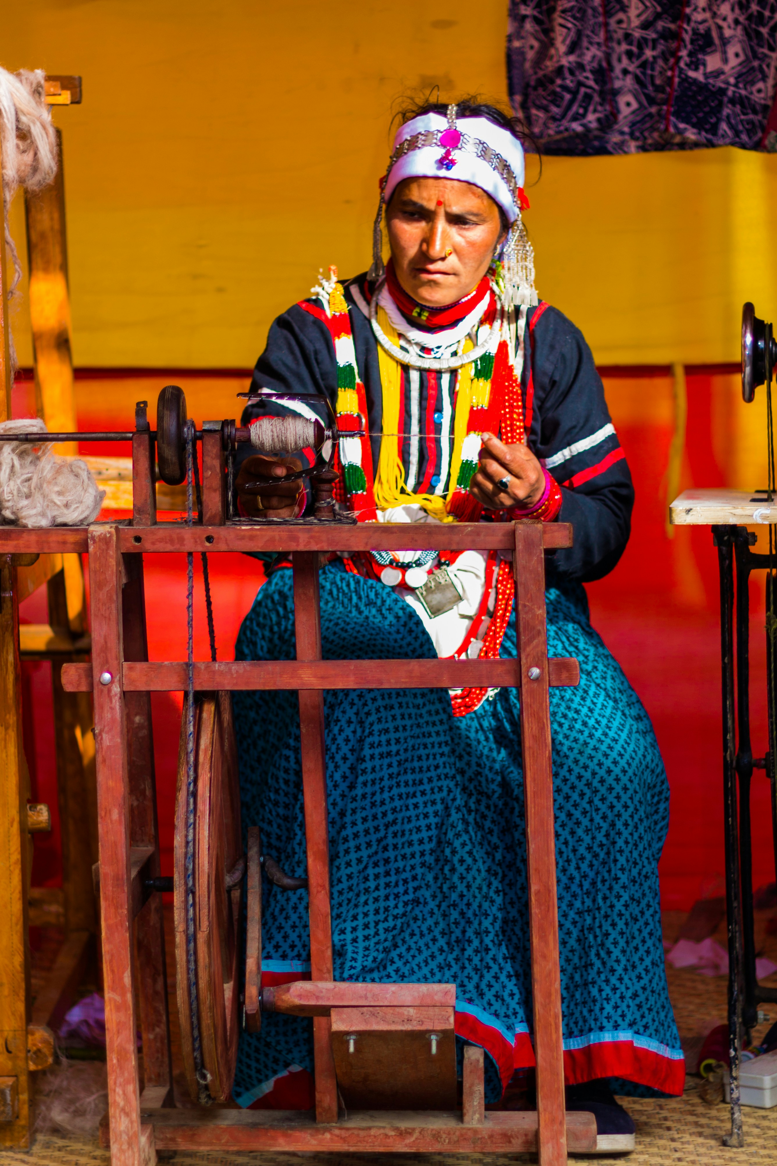Femme en vêtements traditionnels filant du fil sur un rouet en bois.