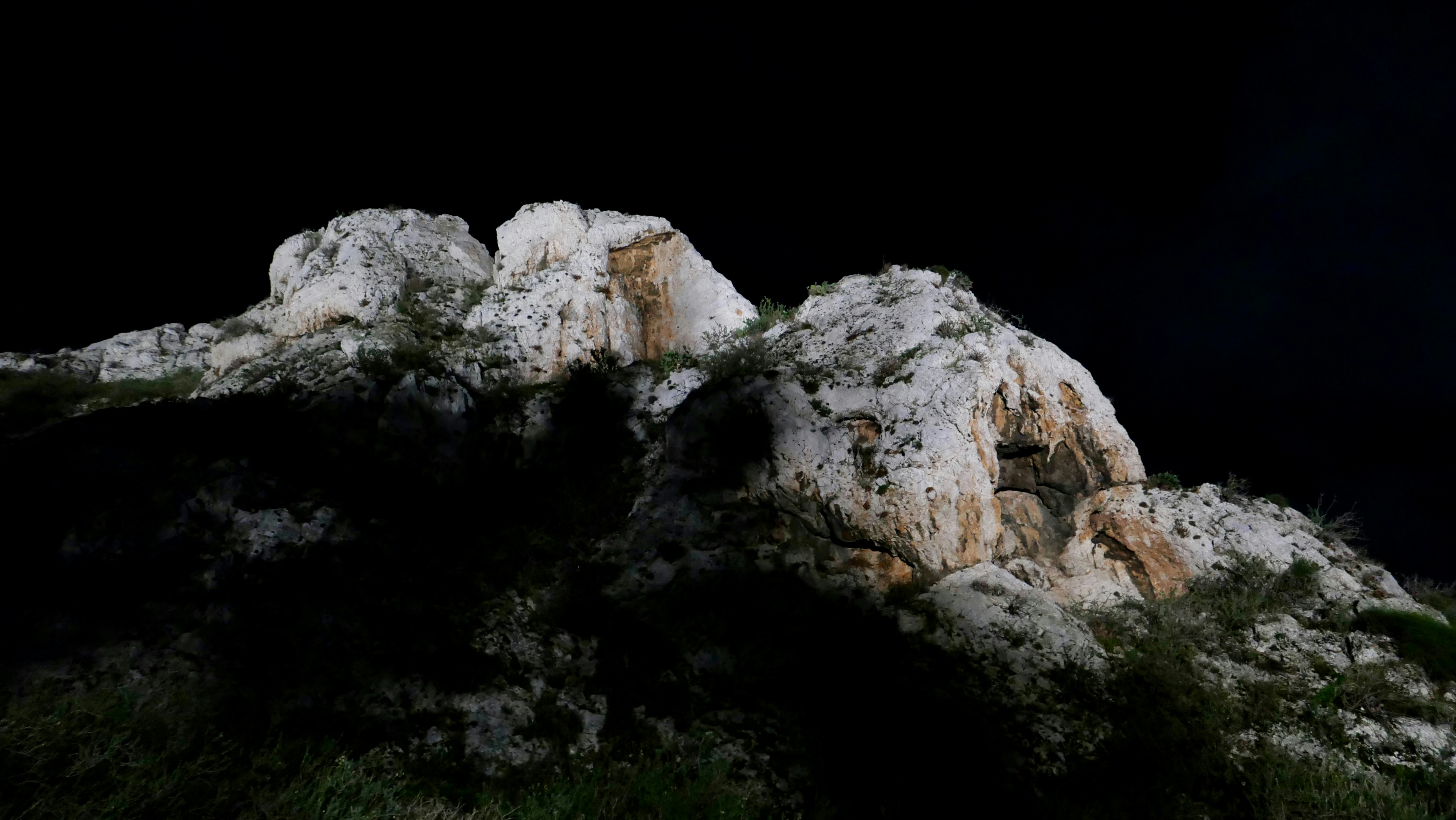 Rocky hill with sparse vegetation against dark sky