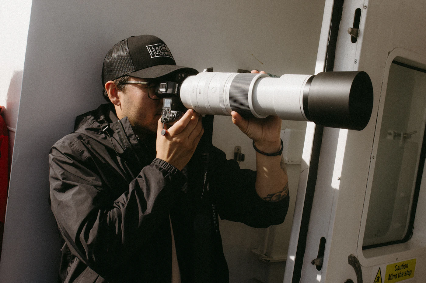 A photographer in a hat aiming a camera with a long telephoto lens