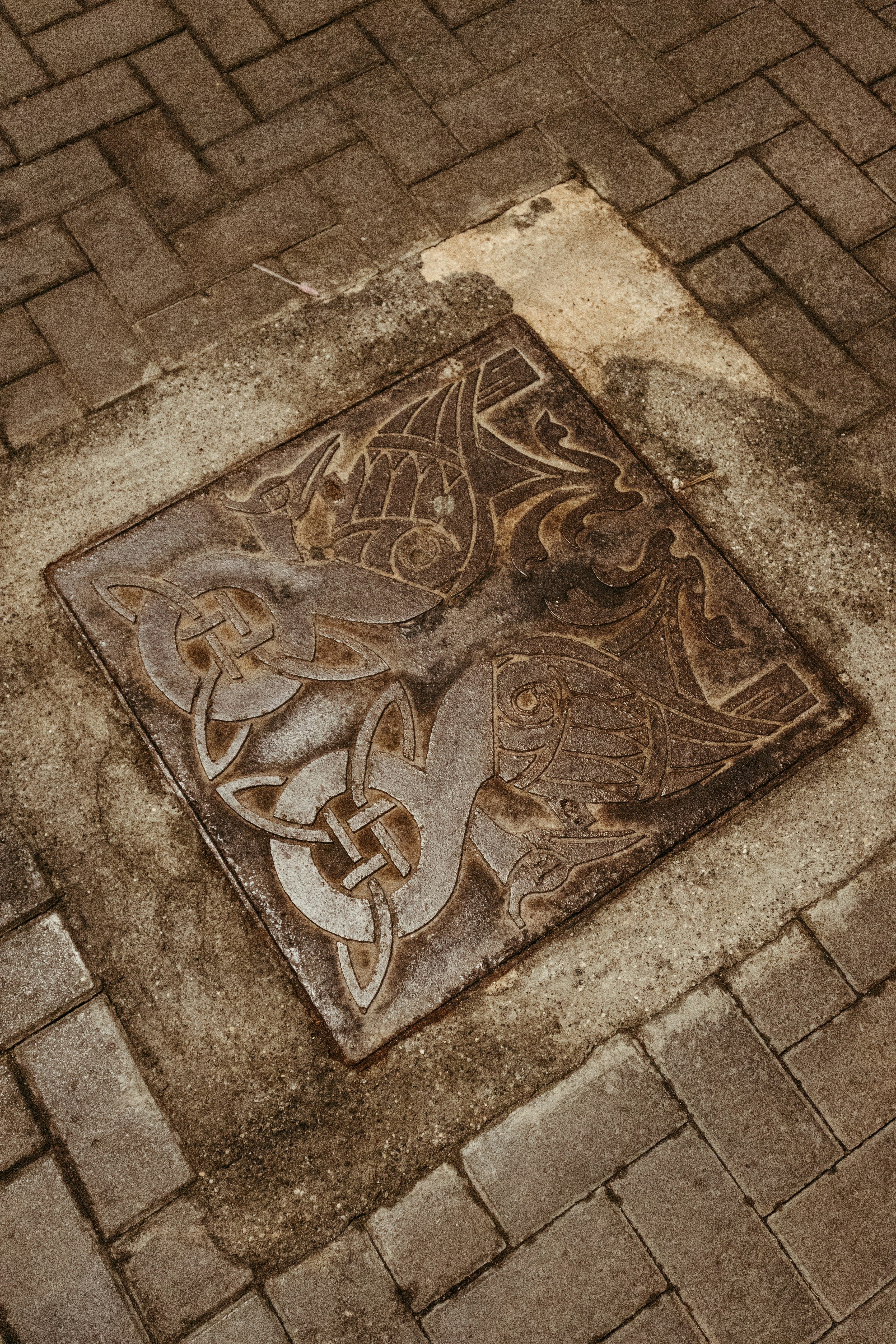 Ornate metal grate with celtic knotwork on brick pavement