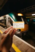 Hand holding train ticket with train in background.