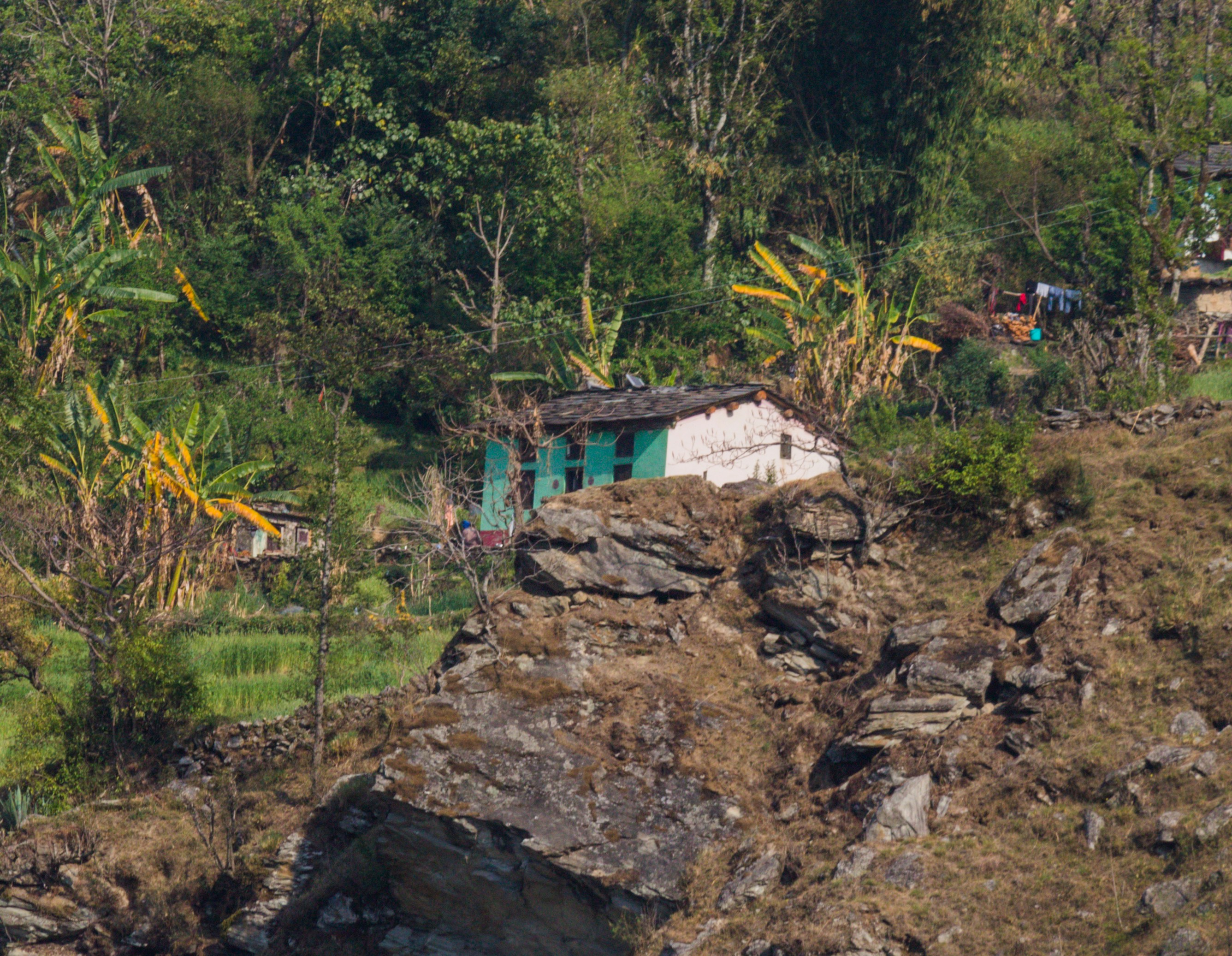 Debris of a village after a massive landslide, showing destroyed houses and a muddy landscape with a few rescue workers in the distance.