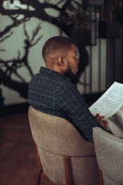 Man in plaid shirt reads document in chair
