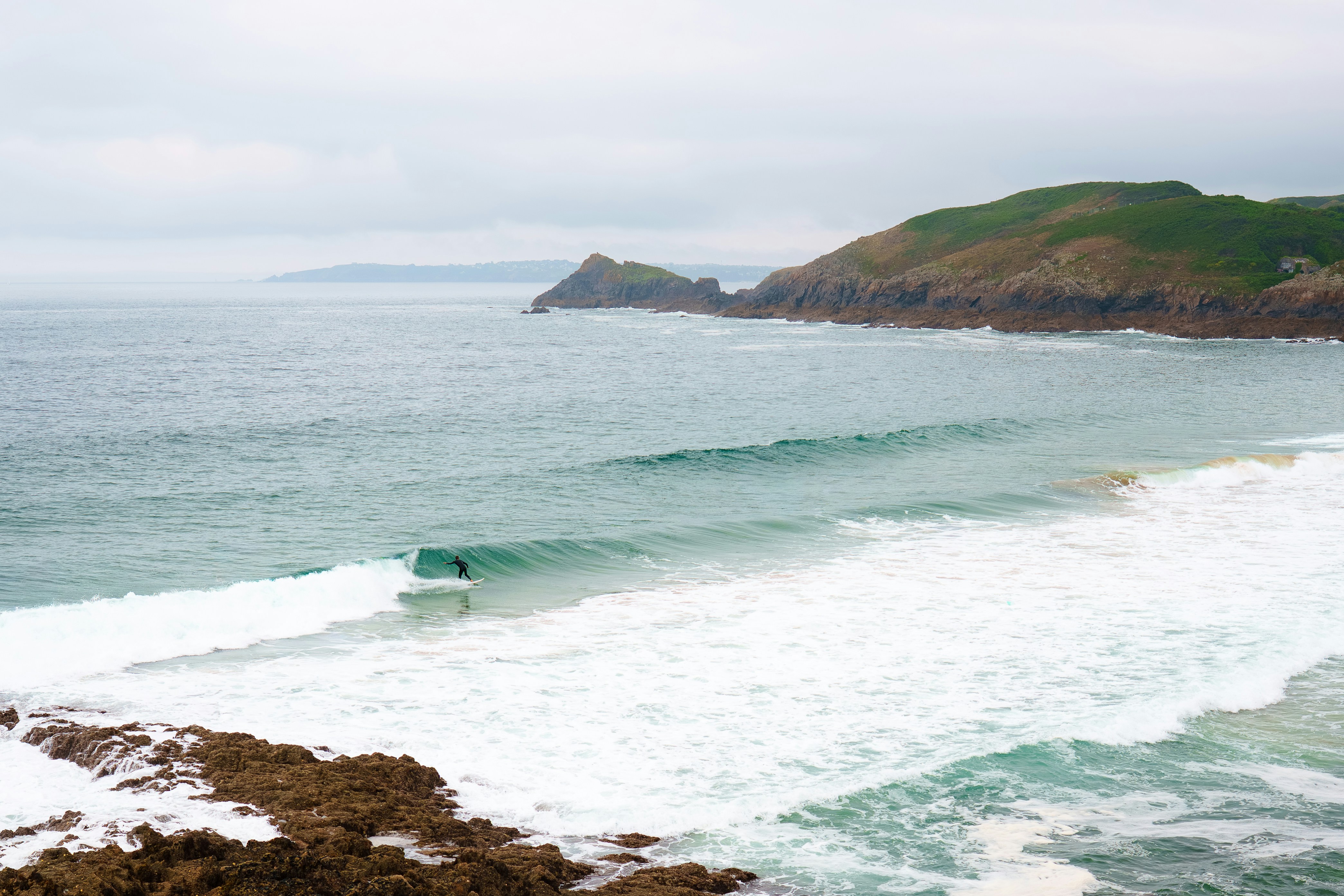 Surfer riding a wave near a rocky coastline.