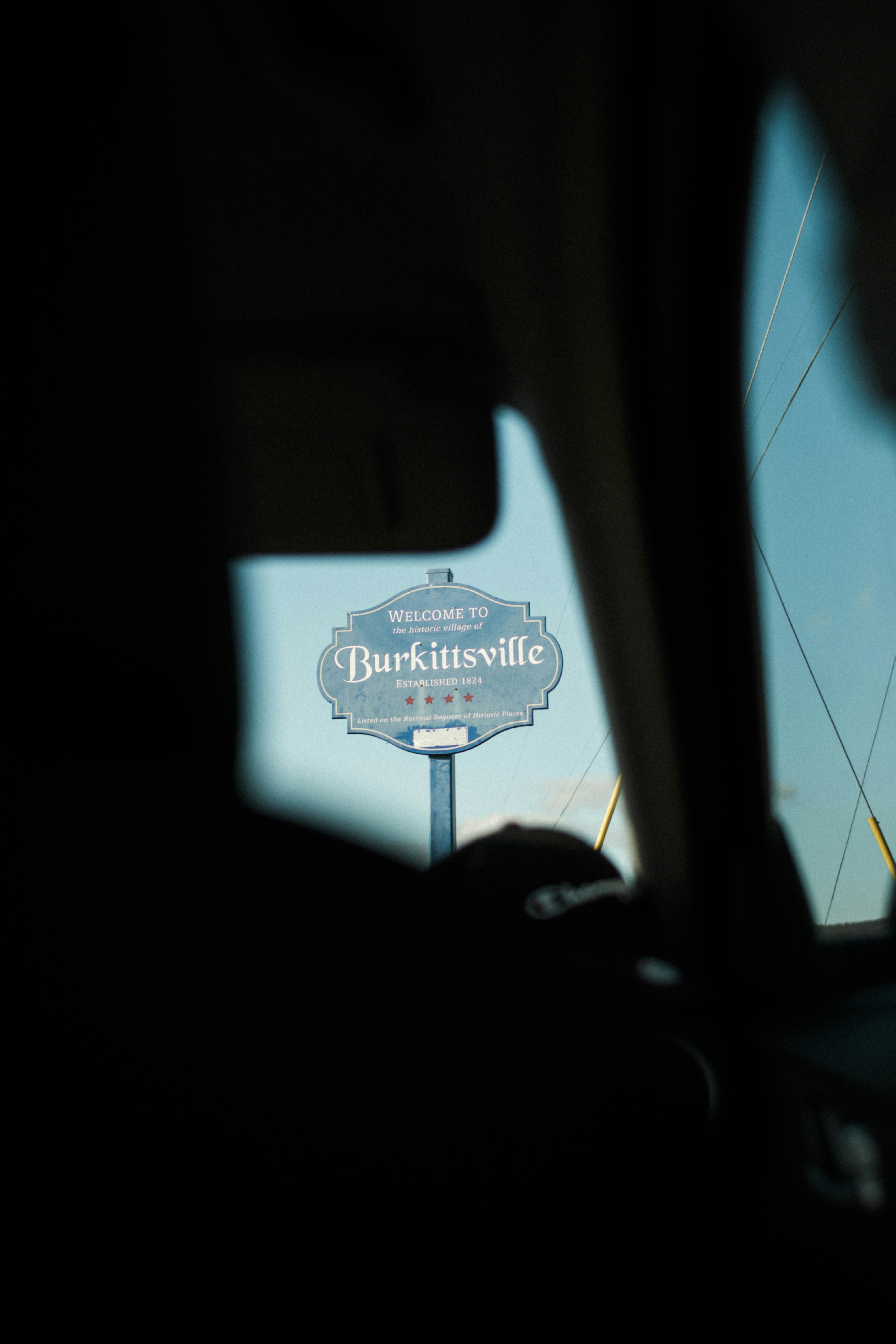 Welcome to burkittsville sign seen through car window