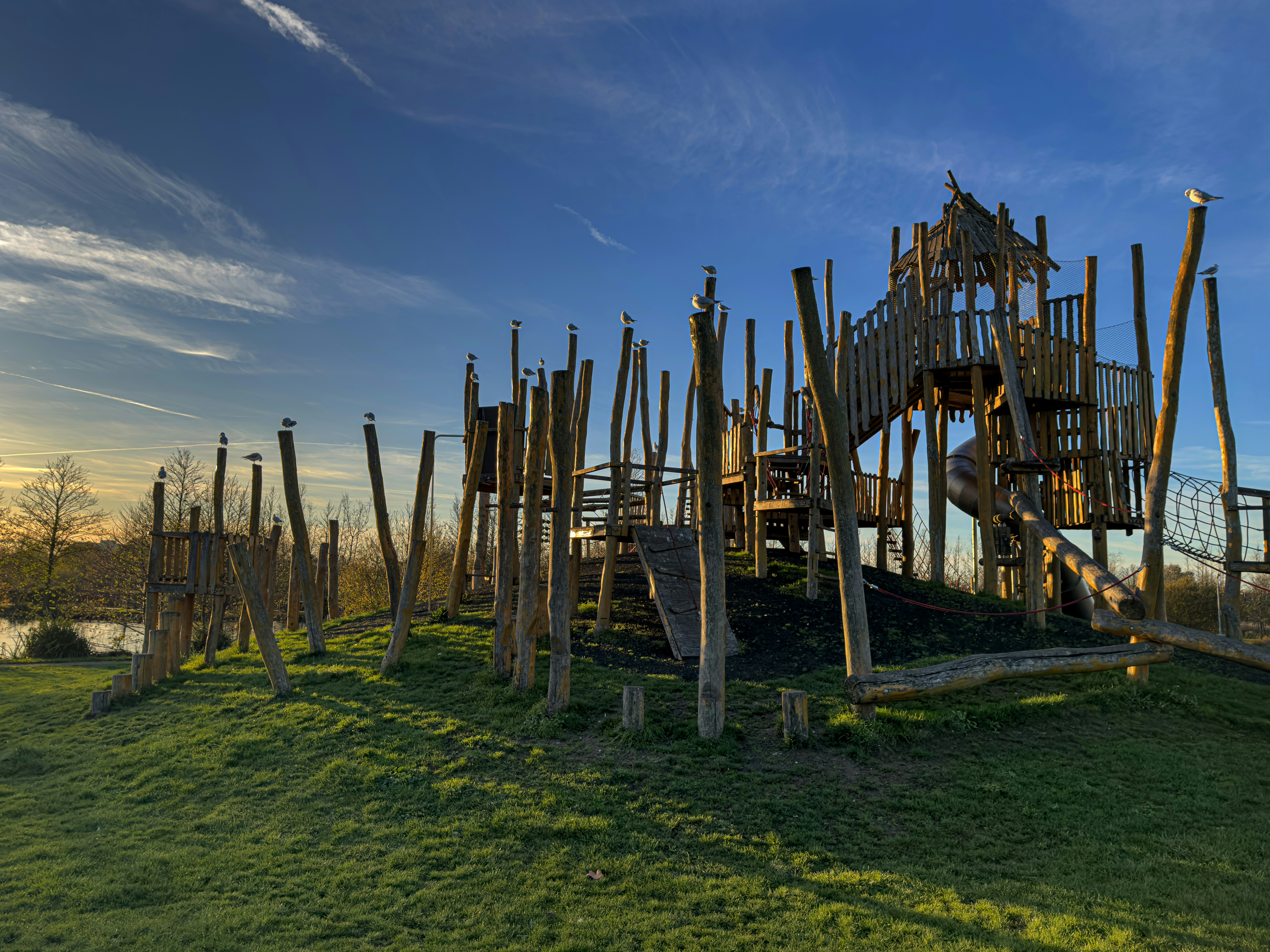 Wooden playground structure on grassy hill under blue sky