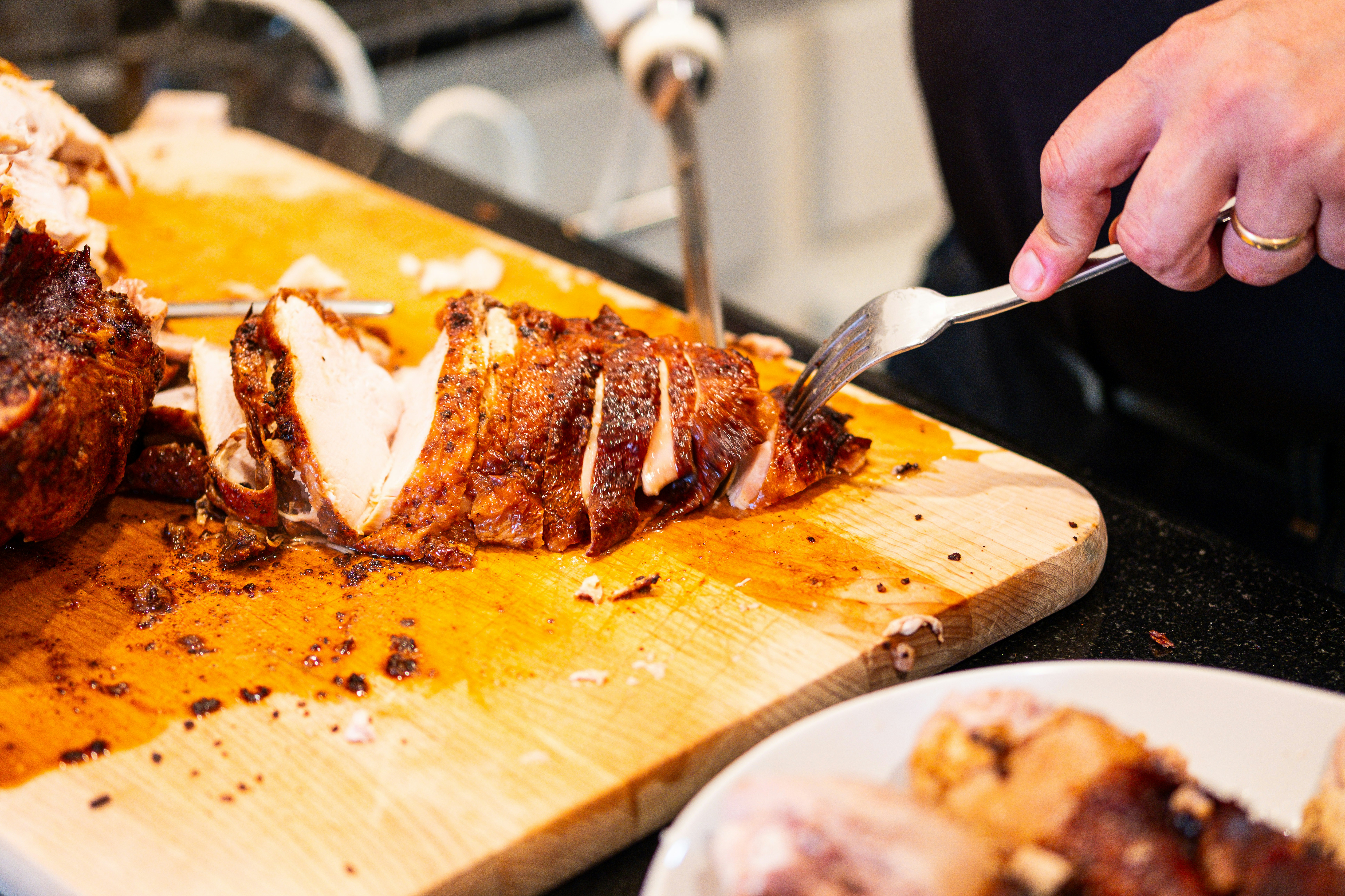 A person carving a roasted chicken on a wooden board