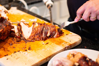 A person carving a roasted chicken on a wooden board