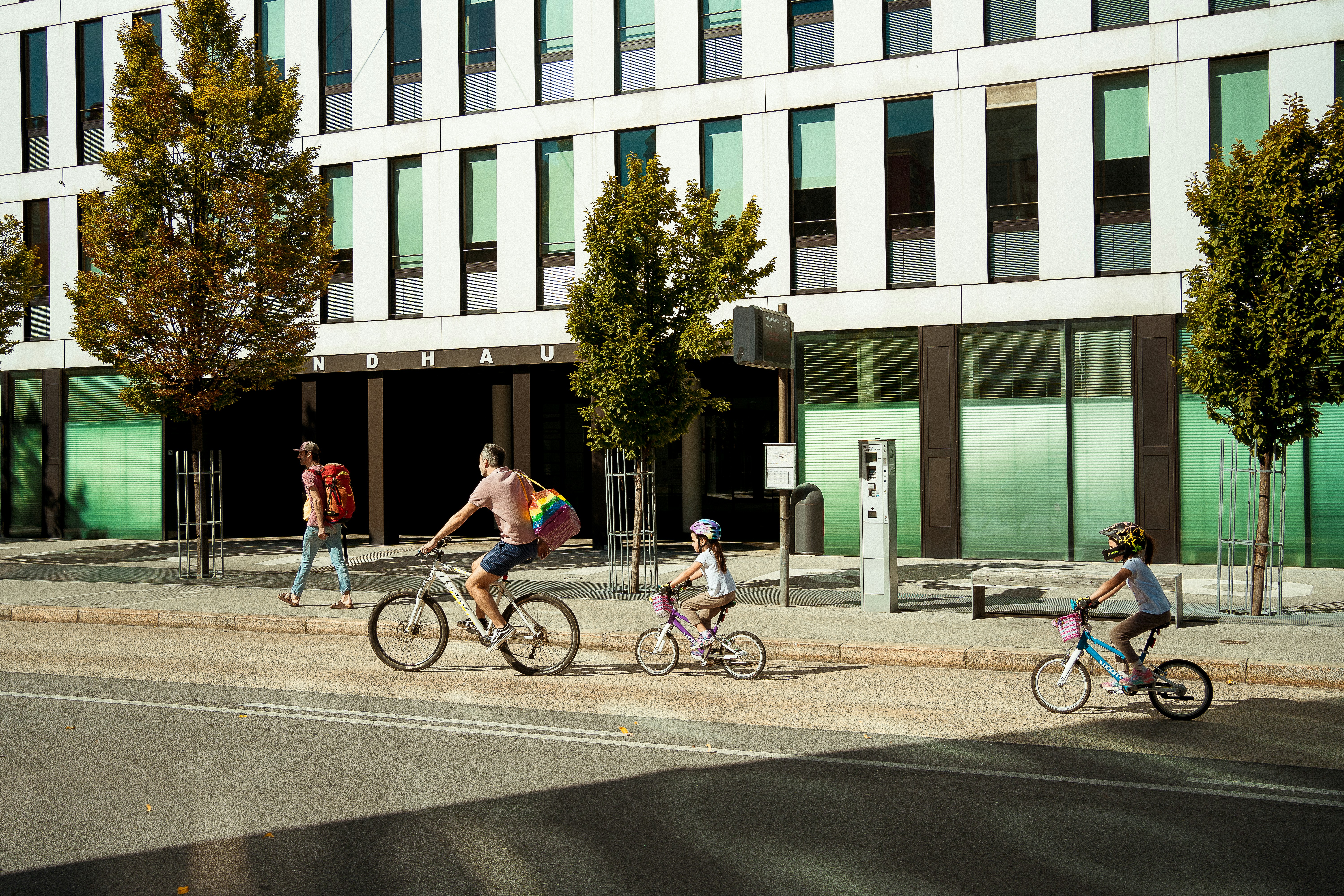 People cycling past a modern building on a sunny day.
