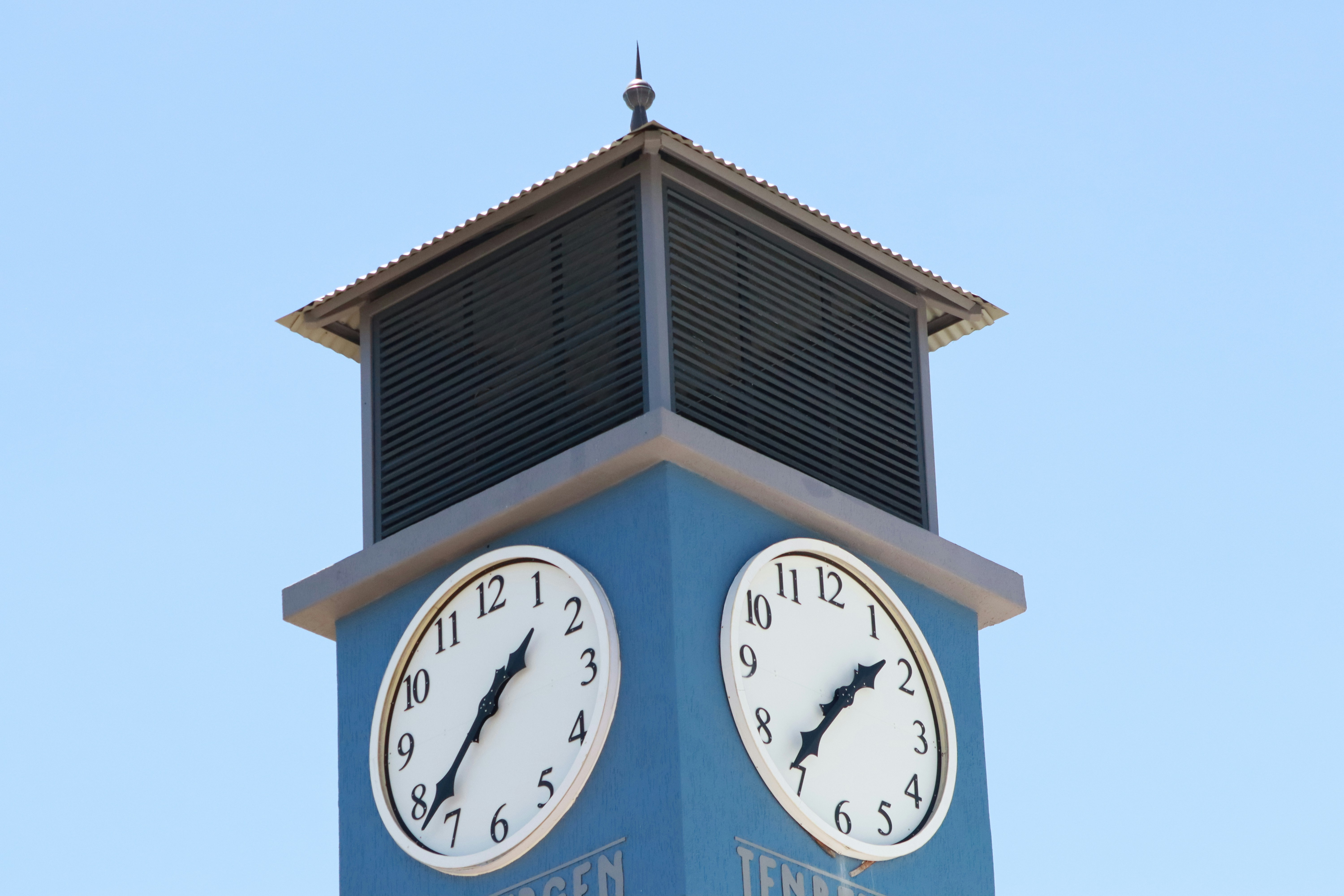 Blue clock tower with two faces against clear sky