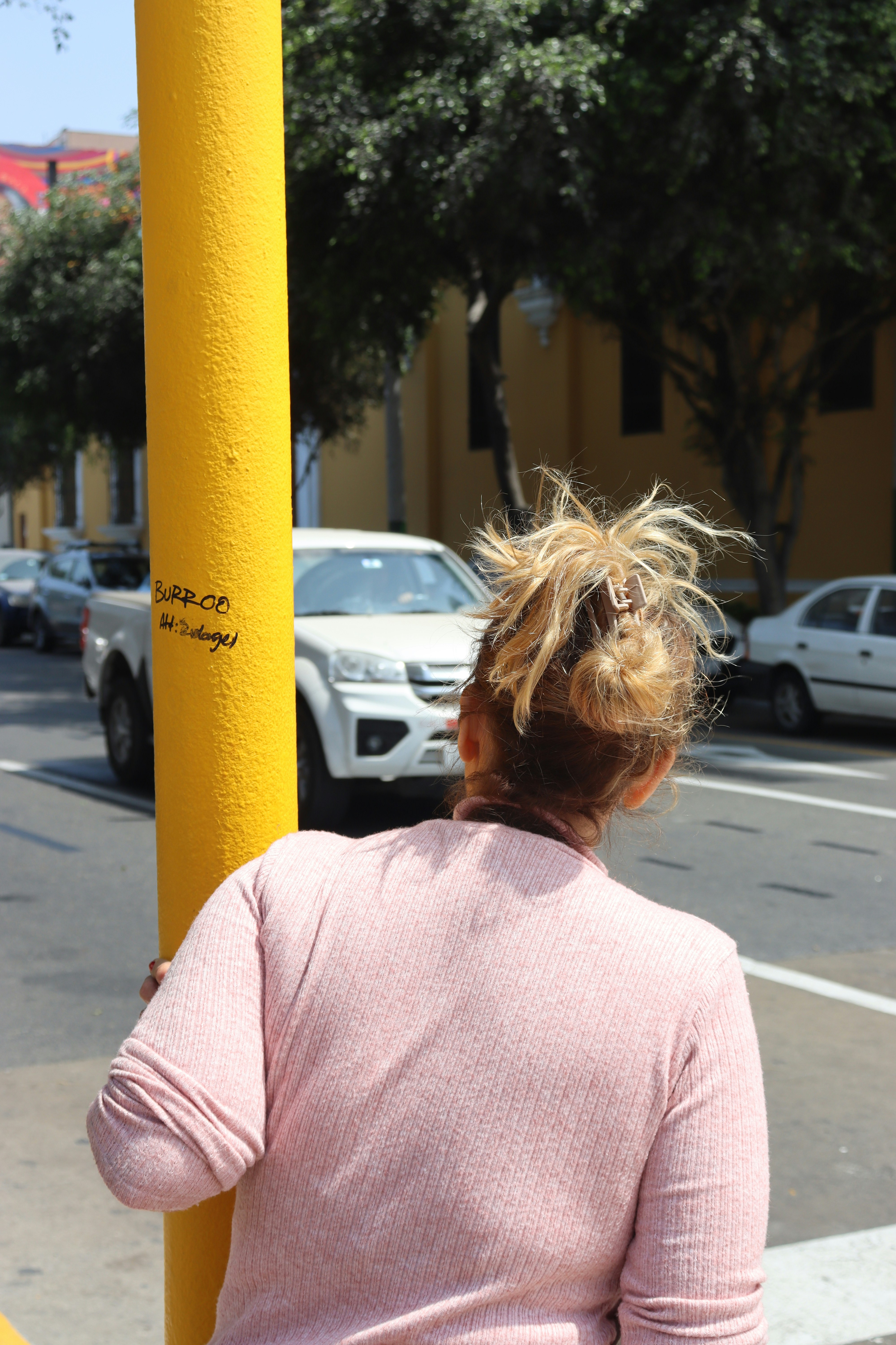 Woman holding onto a yellow pole on a sunny day.