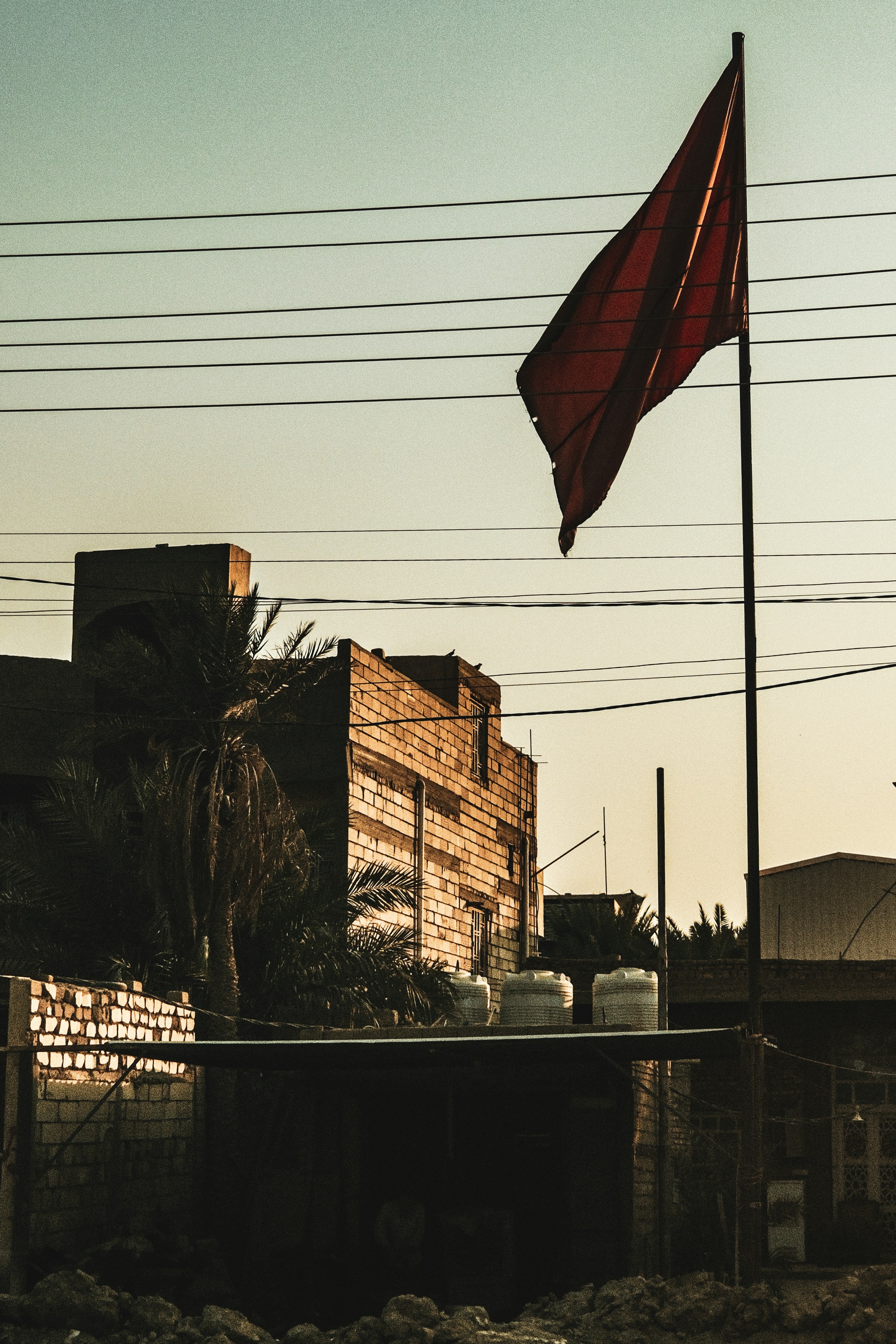 Red flag flies near brick buildings and palm trees