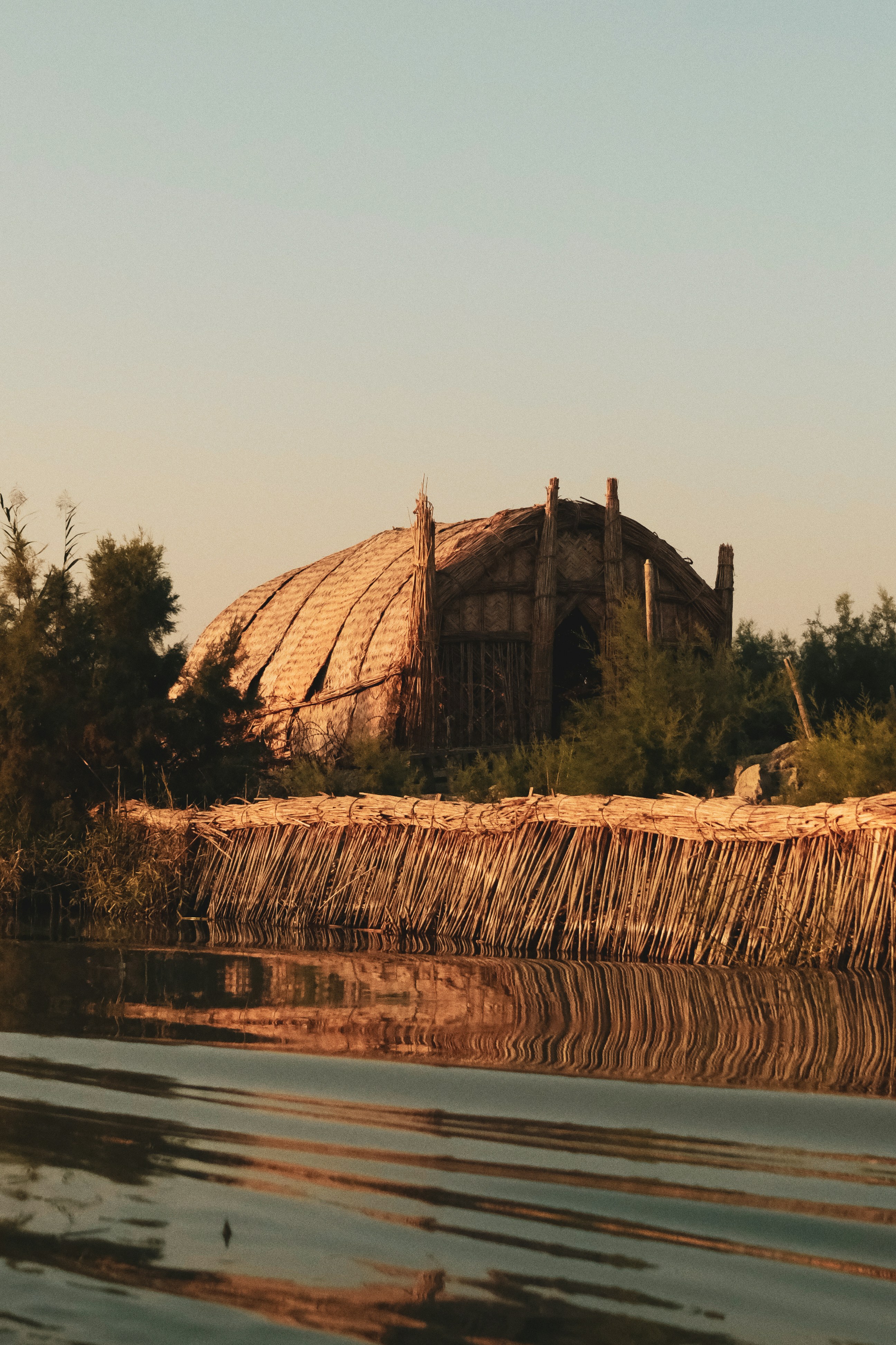Thatched roof building by a calm body of water.