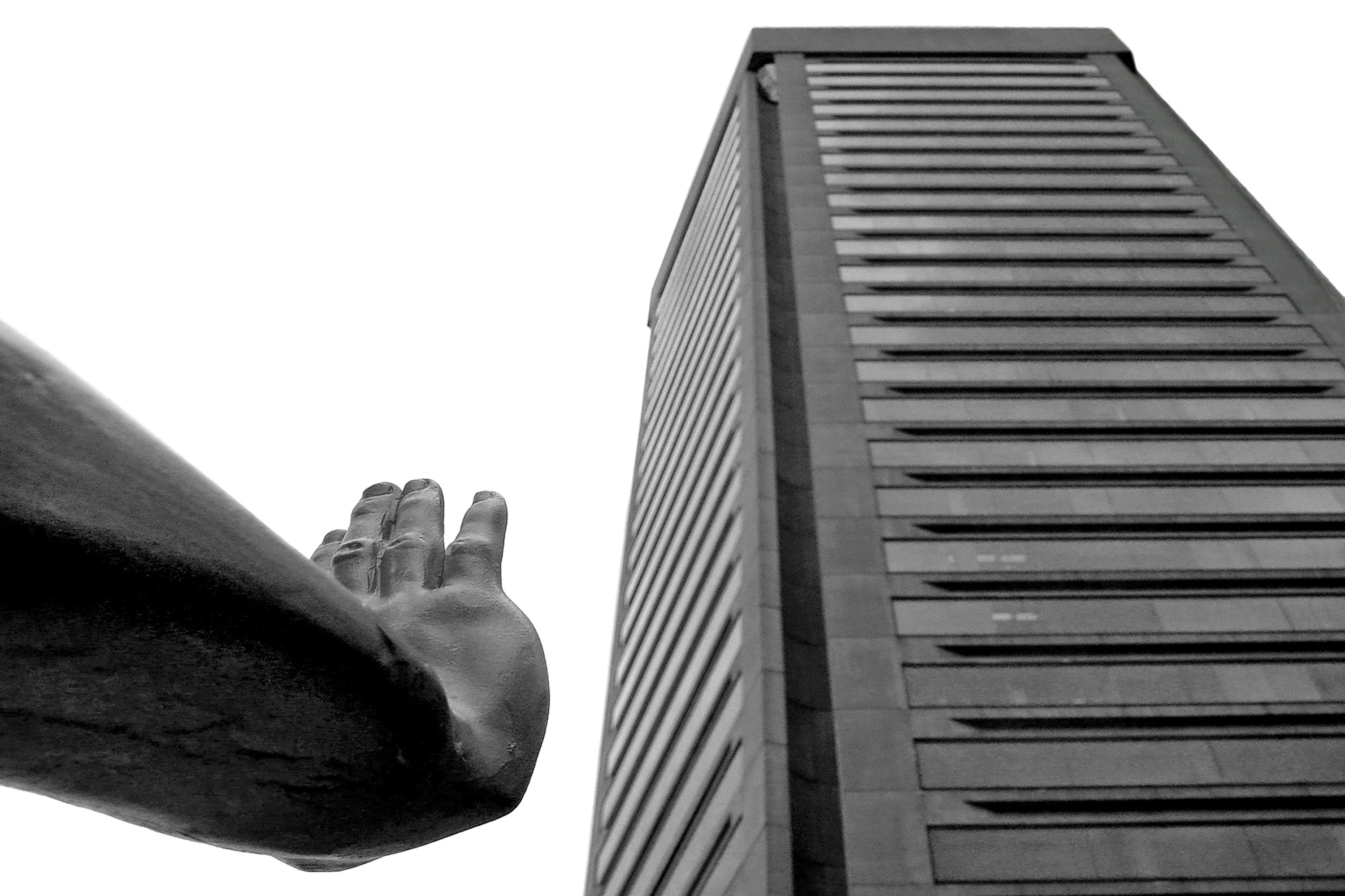A hand reaches towards a tall skyscraper.