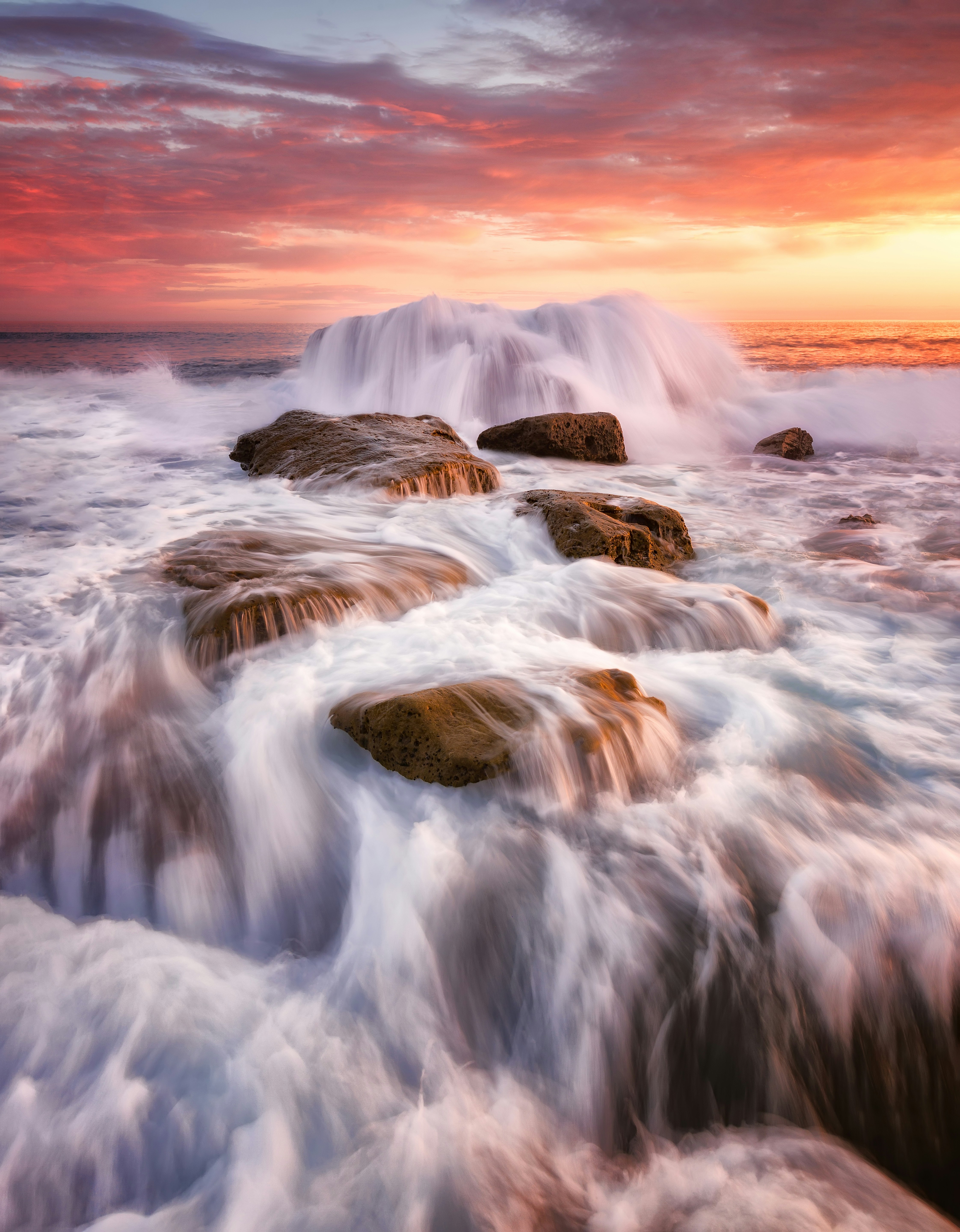 Waves crashing over rocks at sunset