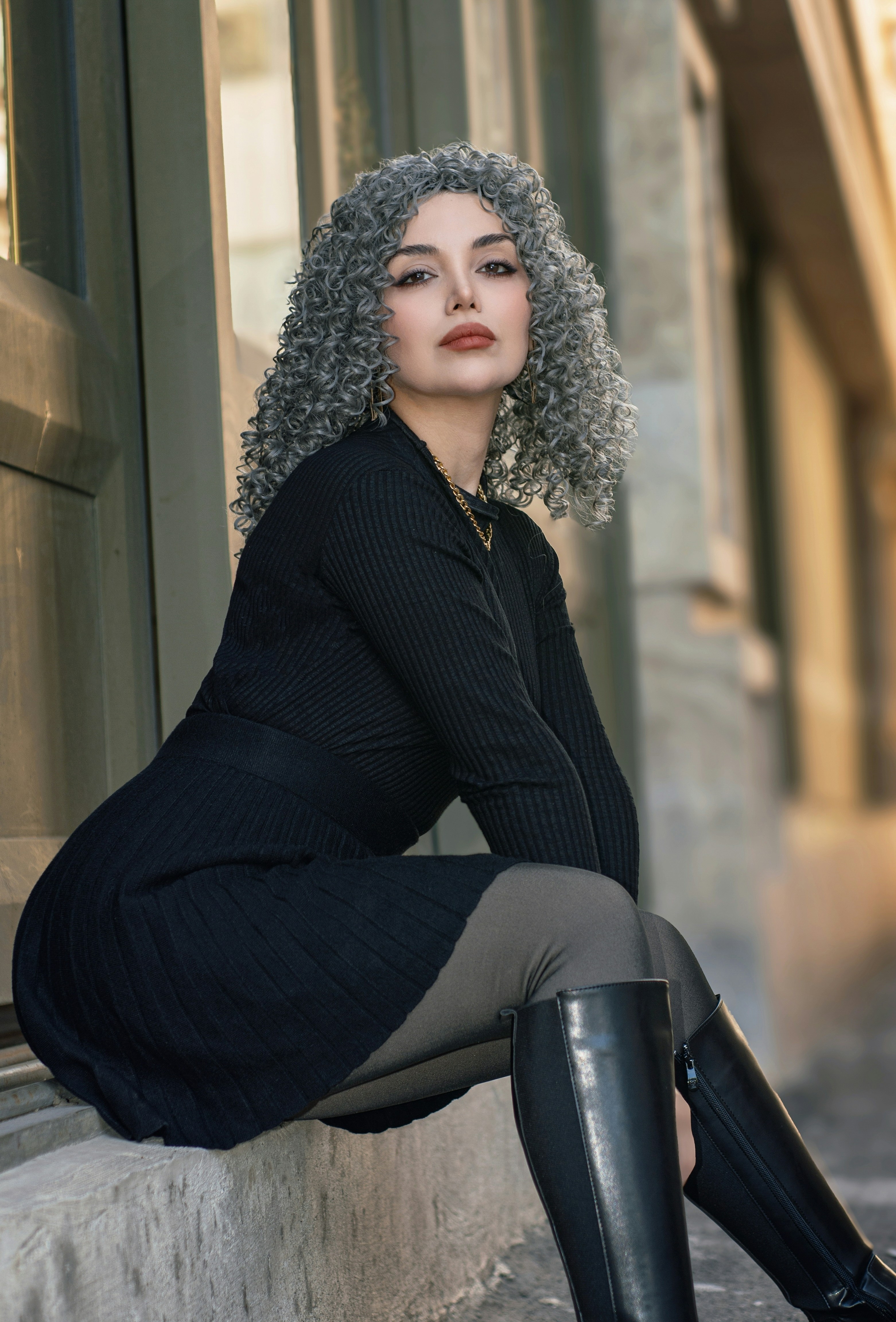 Woman with curly gray hair wearing black dress and boots.