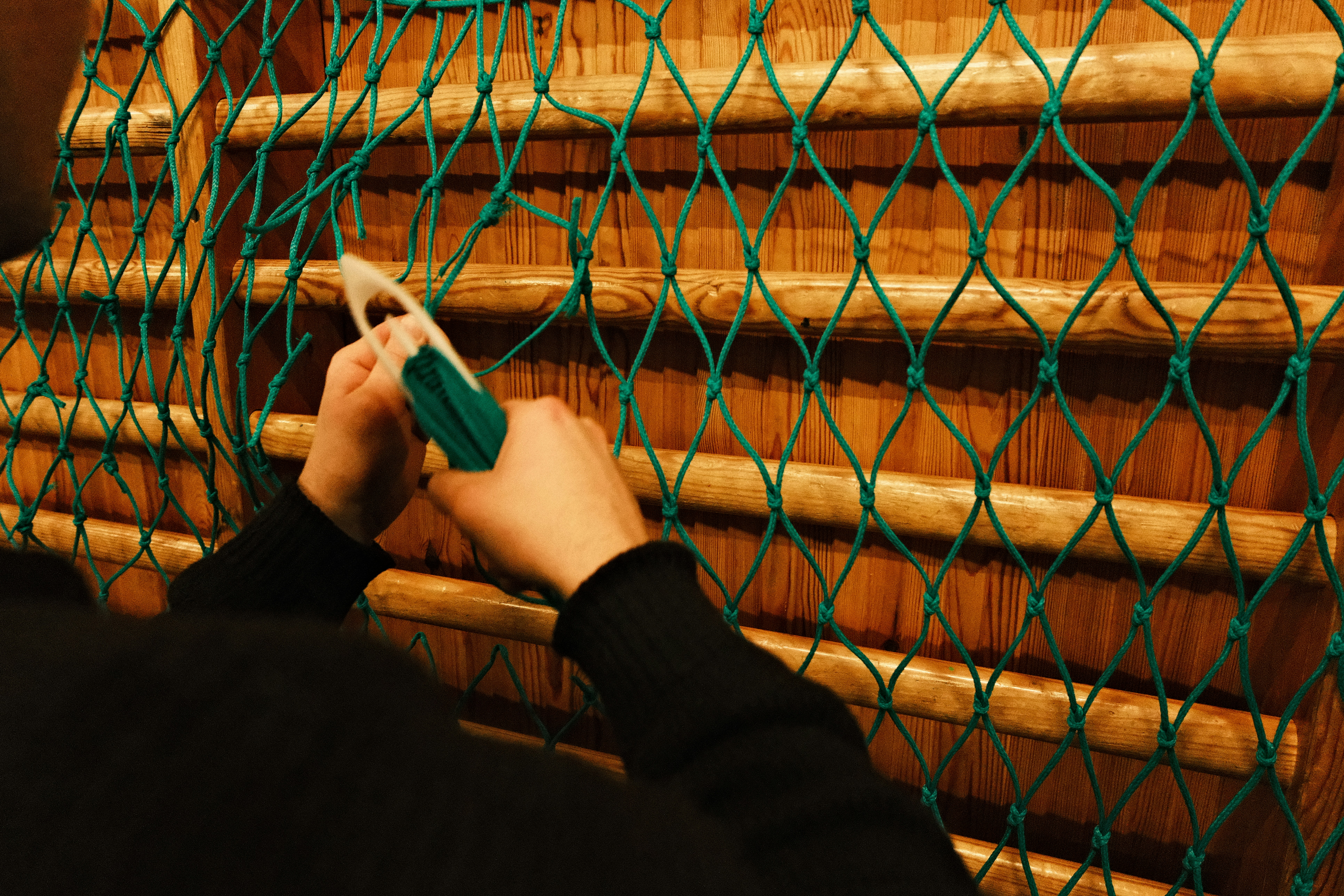 Person's hands tying a knot in a green net.