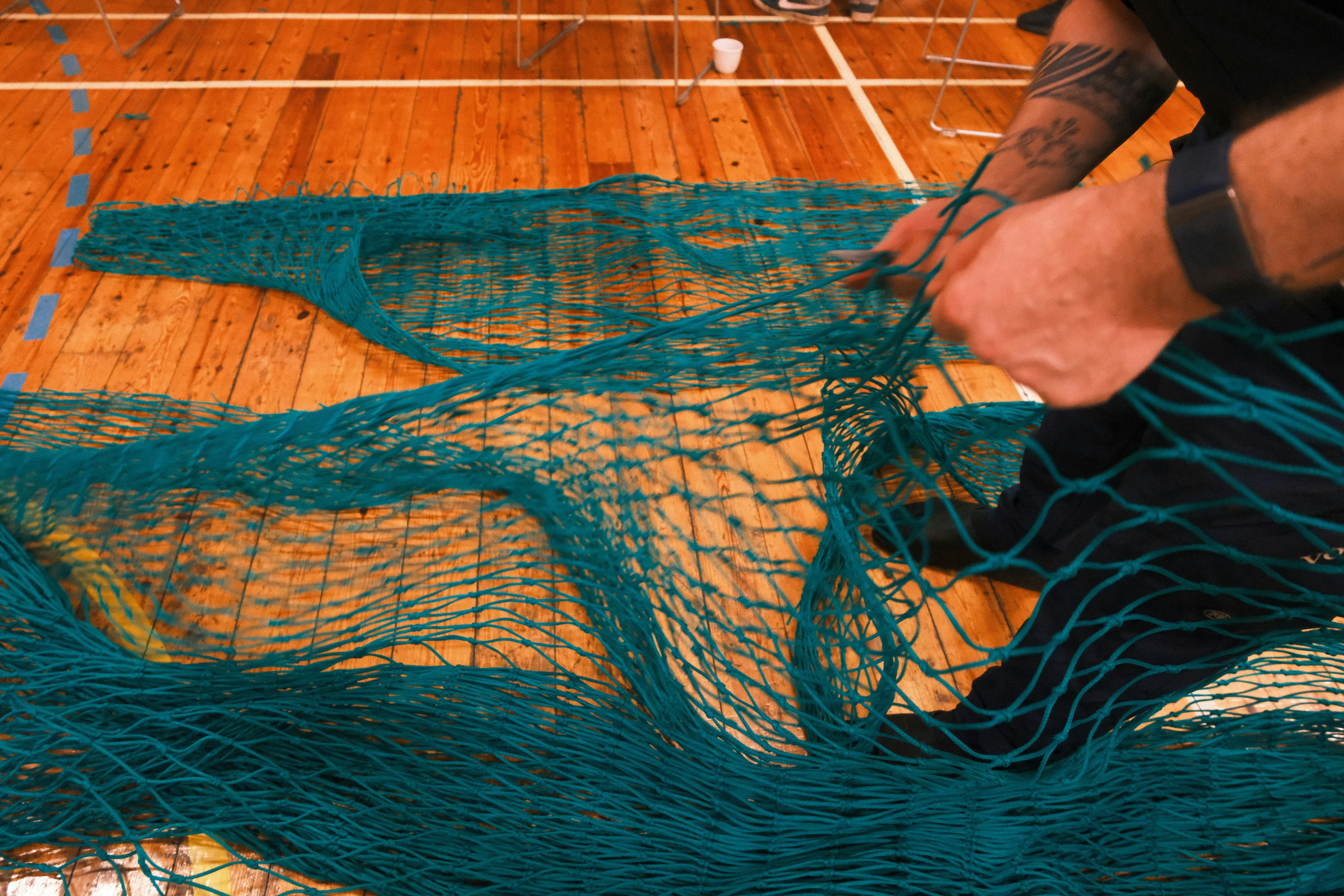 Manos desenredando una red verde en un suelo de madera.