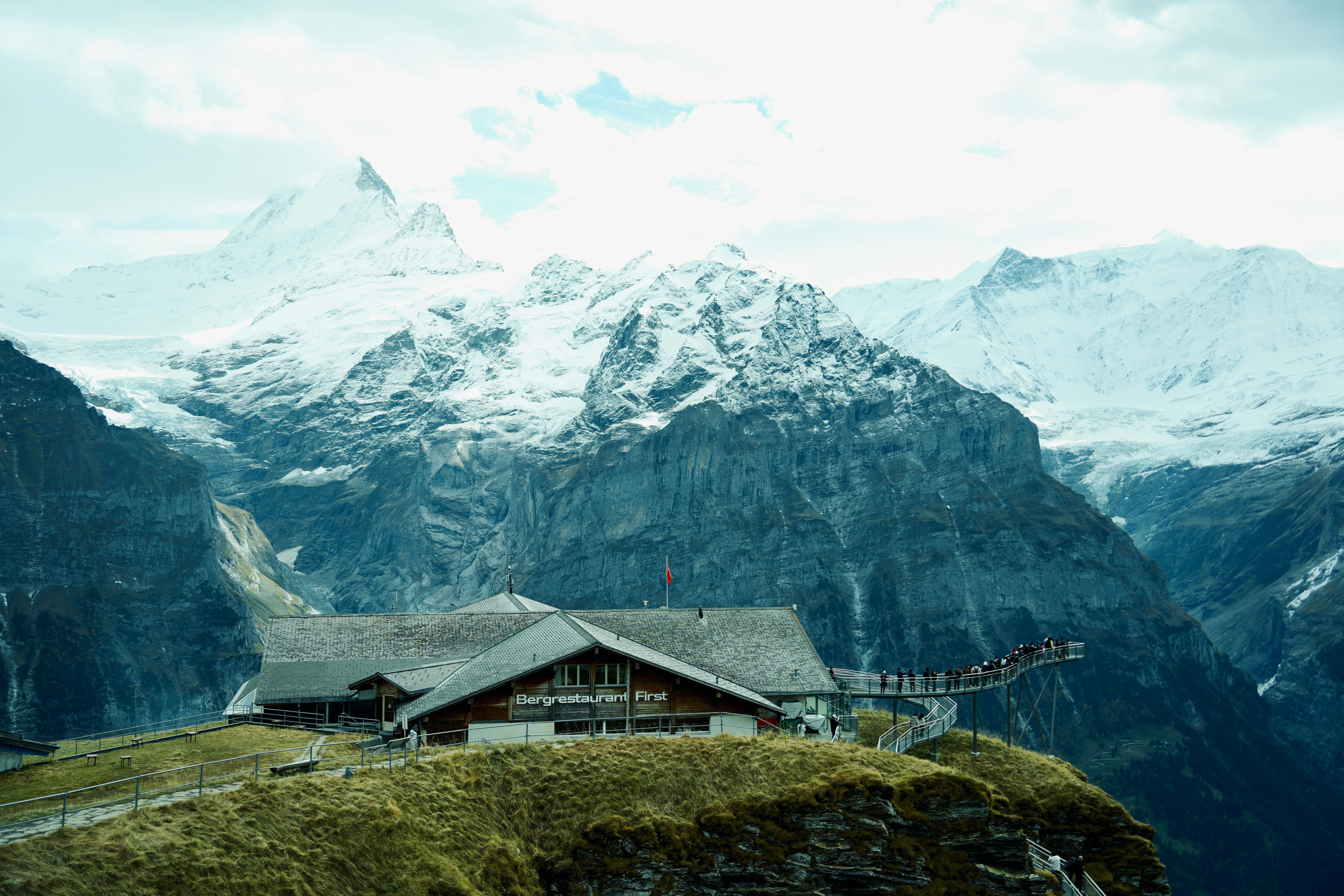 A lodge sits on a hill with snowy mountains behind.