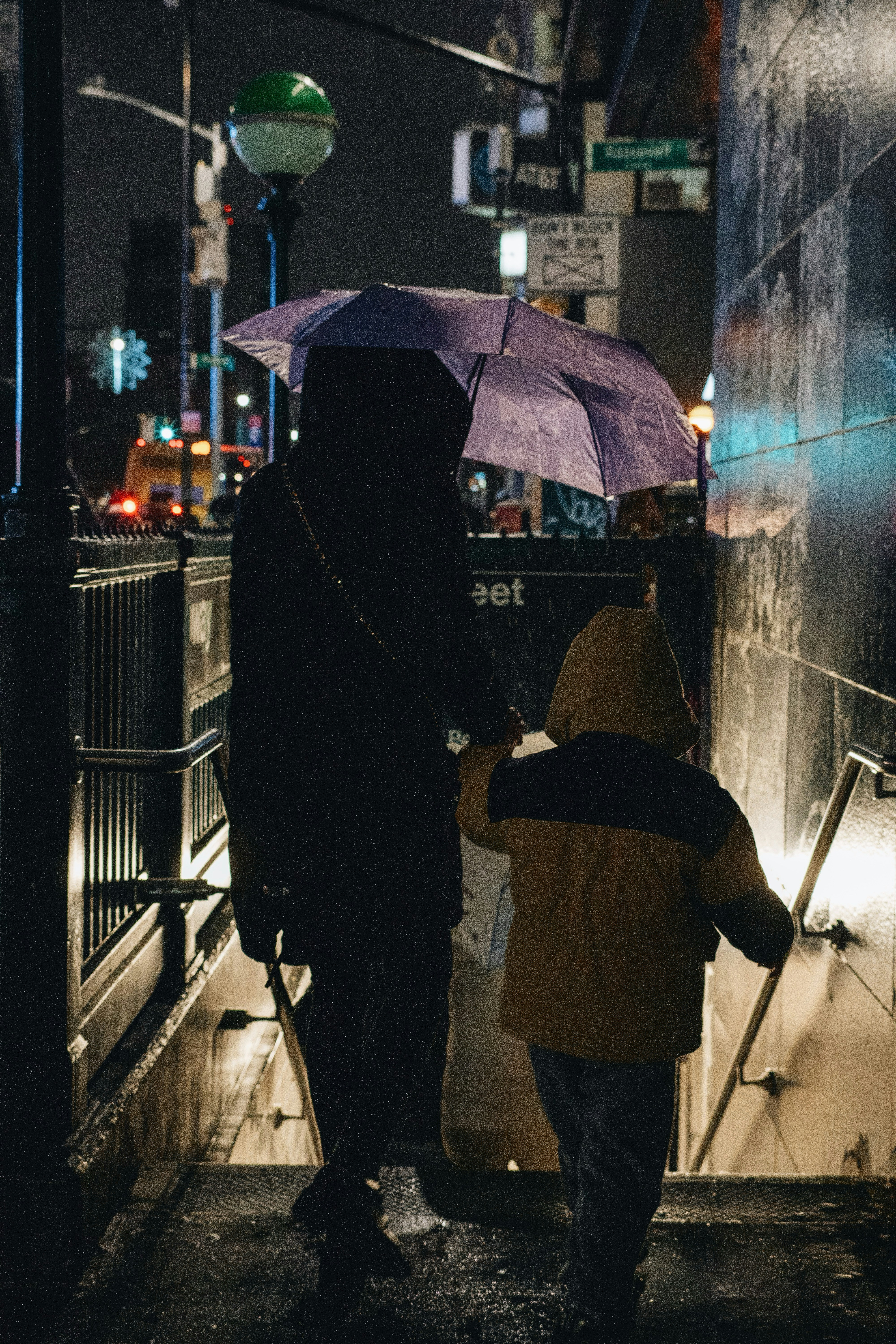 Persona con un paraguas con un niño entrando en el metro por la noche.