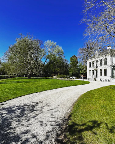 White manor house with gravel driveway and green lawn