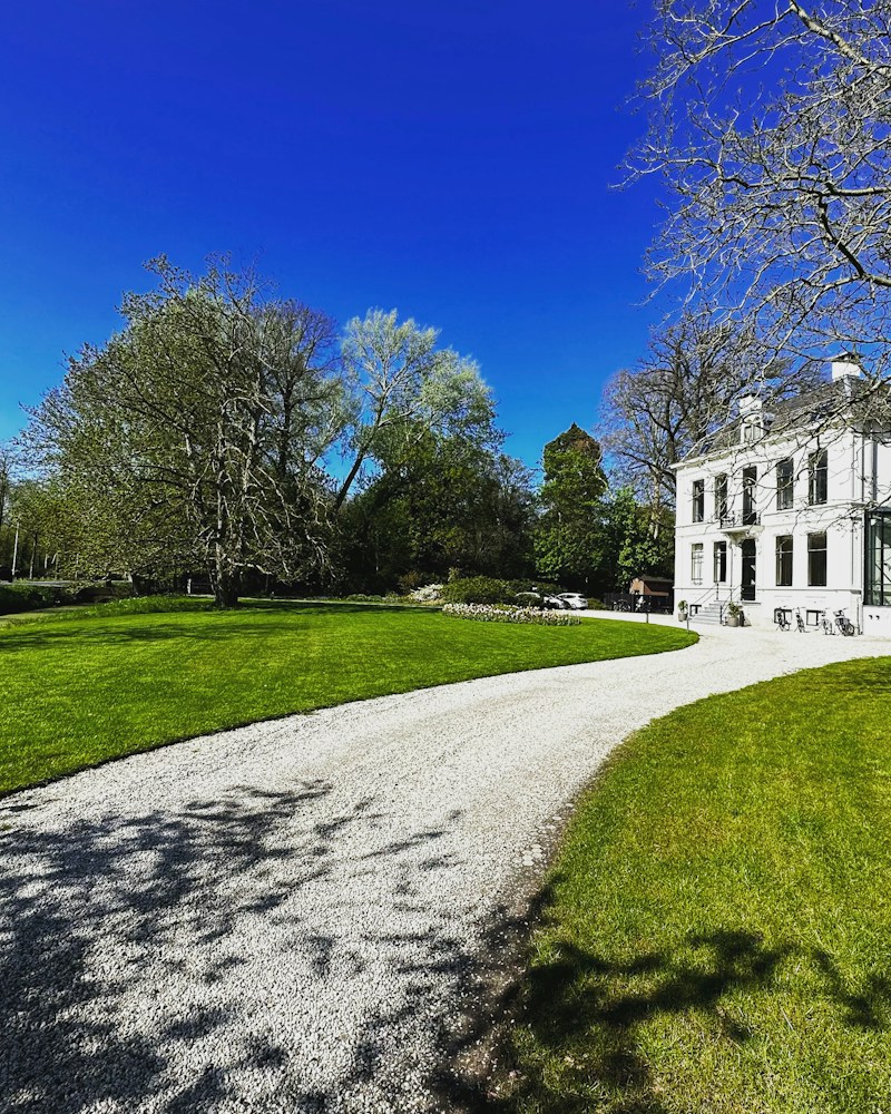 Pale gravel driveway sweeping across a lawn to a white manor house