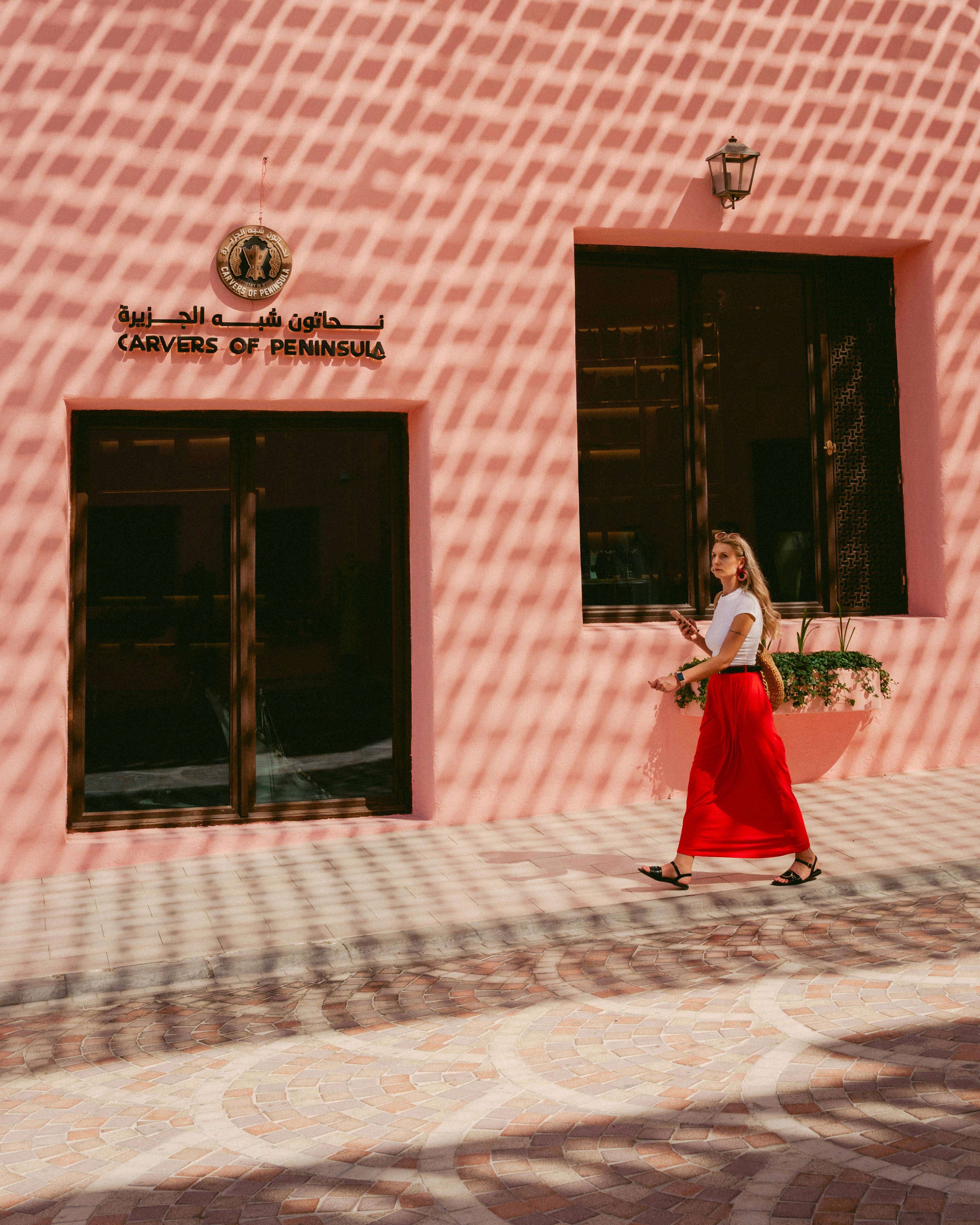 Woman in red skirt walks past pink building