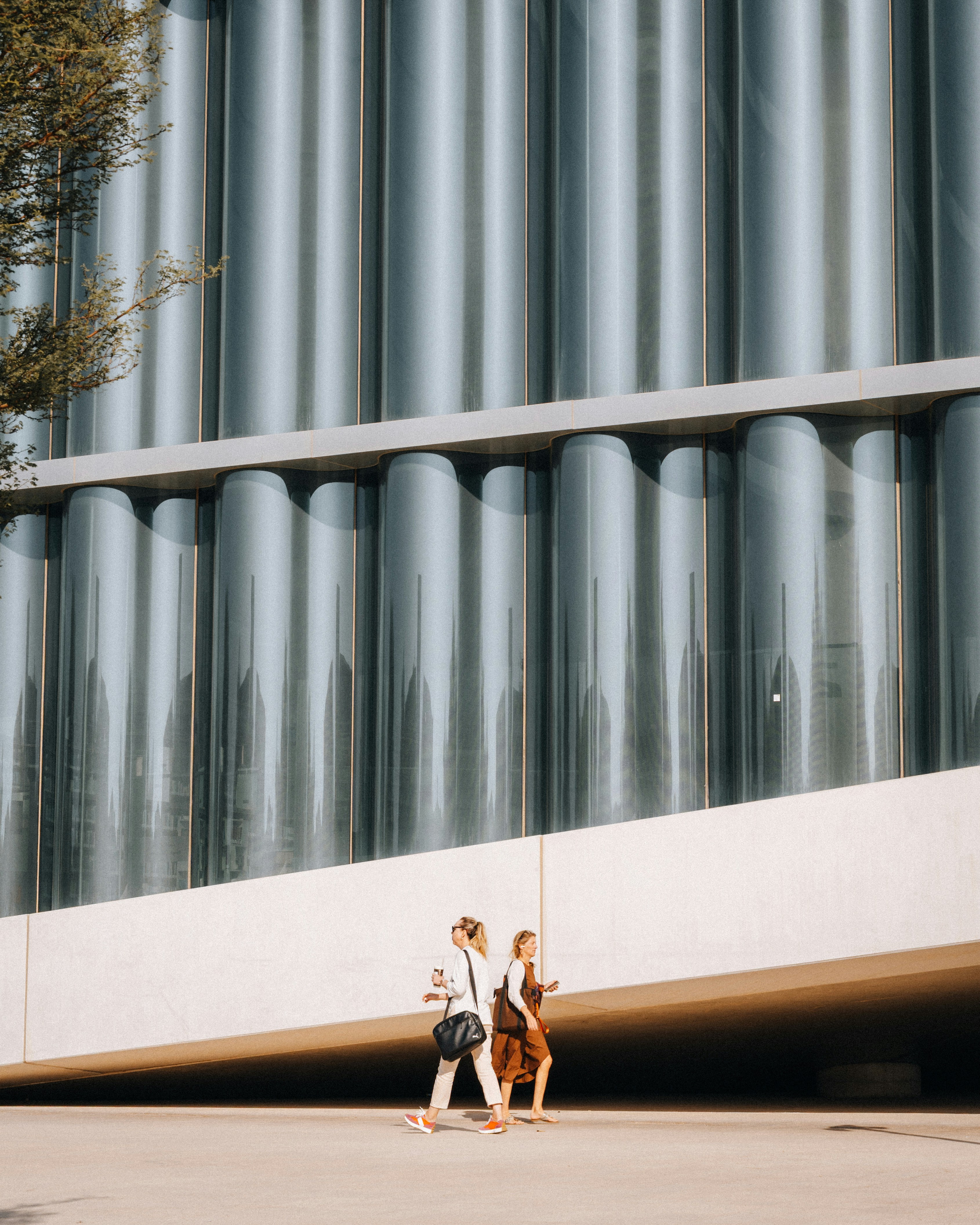 Two women walk past a modern building with glass facade.