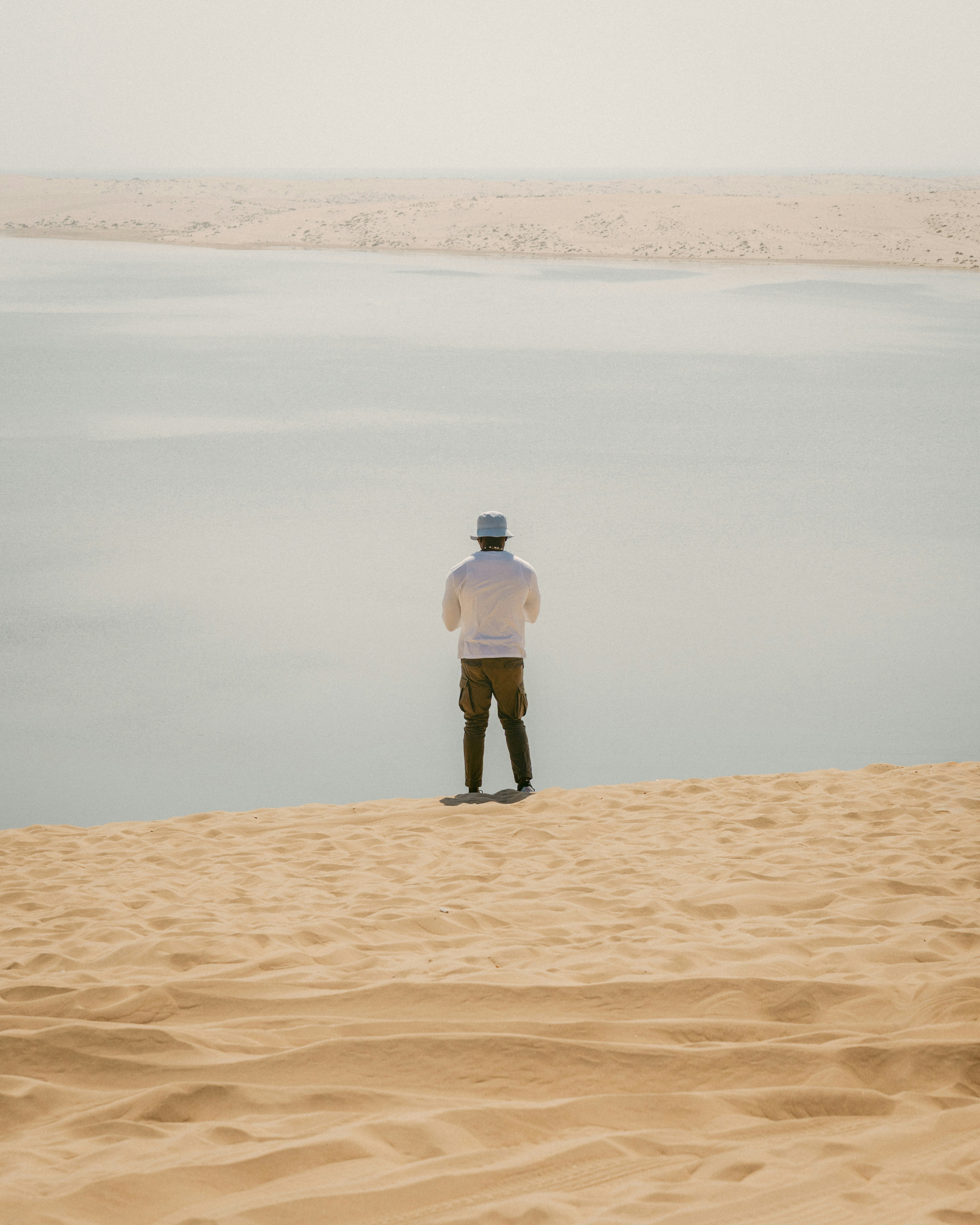Man standing on sand dune overlooking water